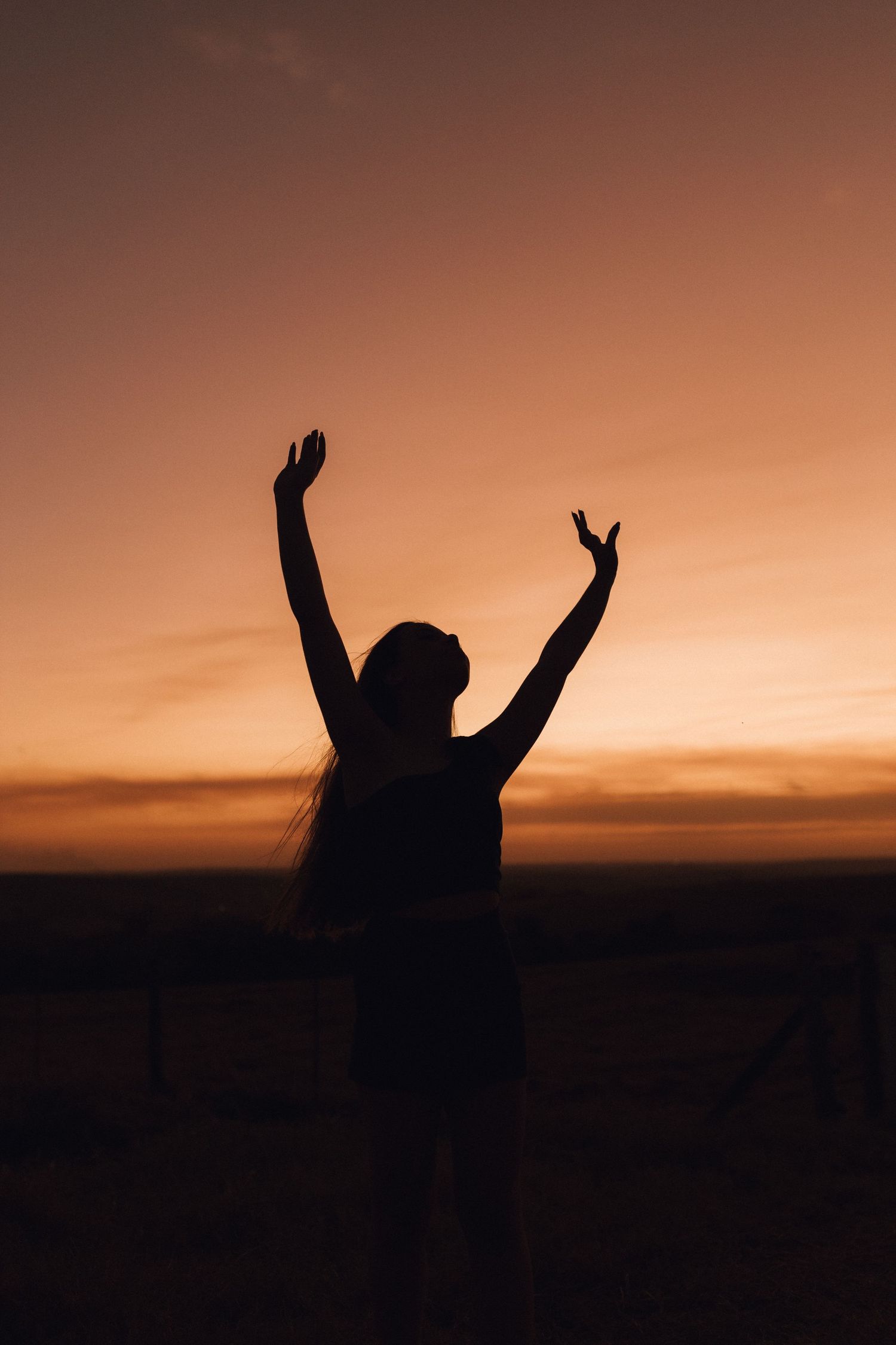 Silhouette of a woman with arms raised against a vibrant orange sunset sky.