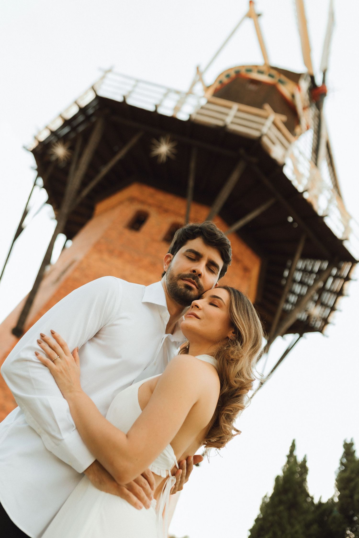 Couple embracing tenderly in front of a historic windmill at sunset.