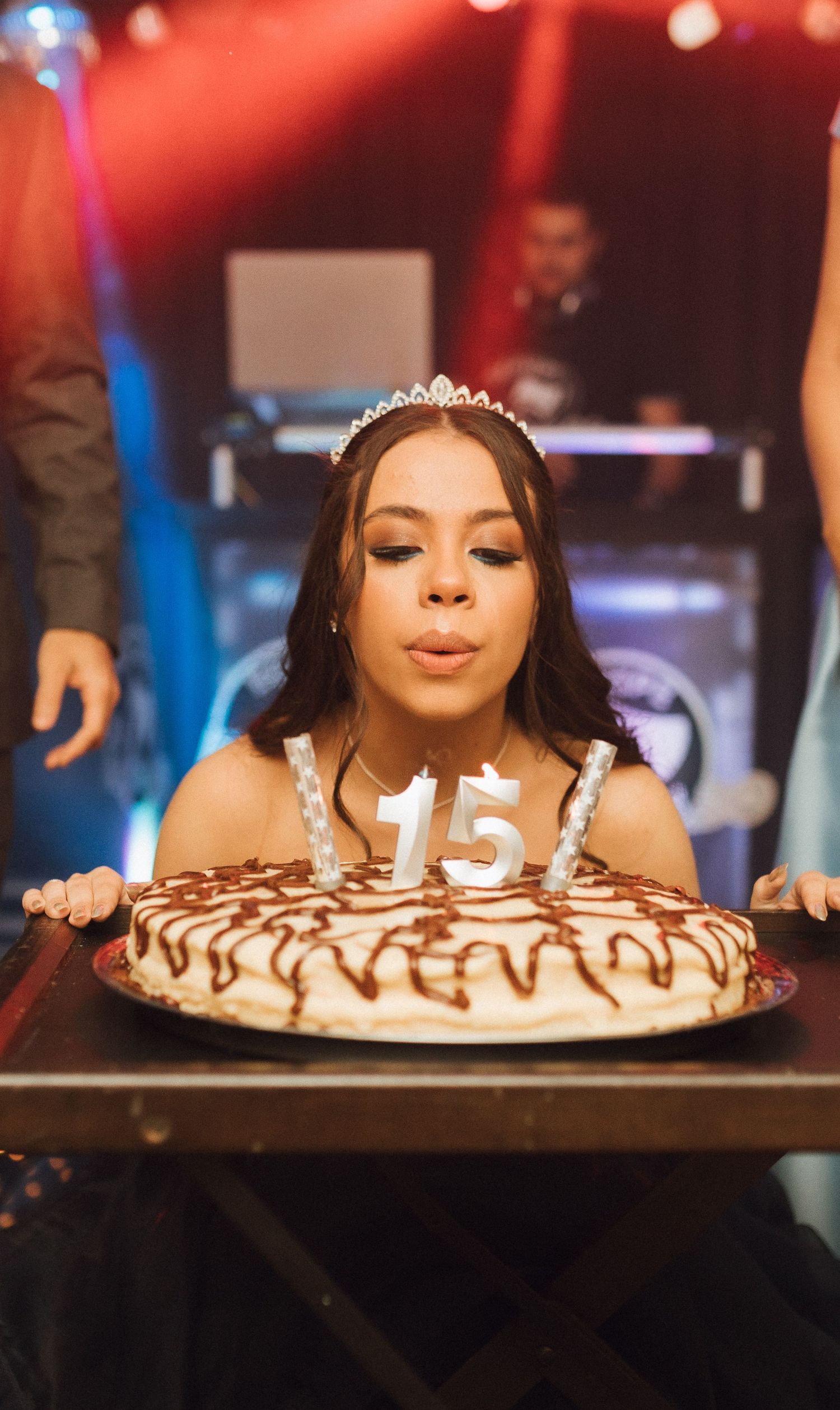 Teen girl in tiara blows out number 15 candles on birthday cake at her quinceañera celebration.