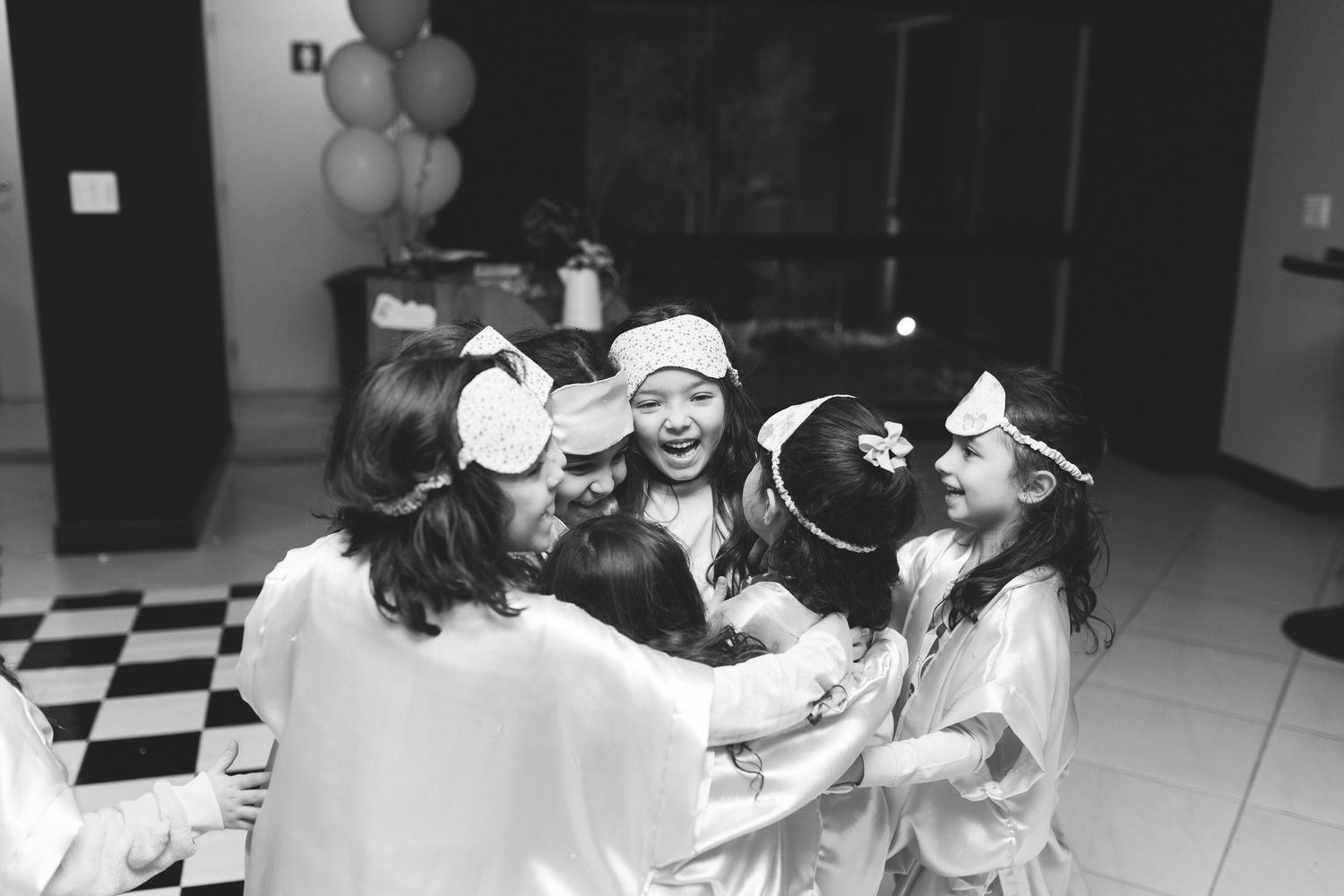 Black and white photo of girls in robes and sleep masks hugging at a fun sleepover party.