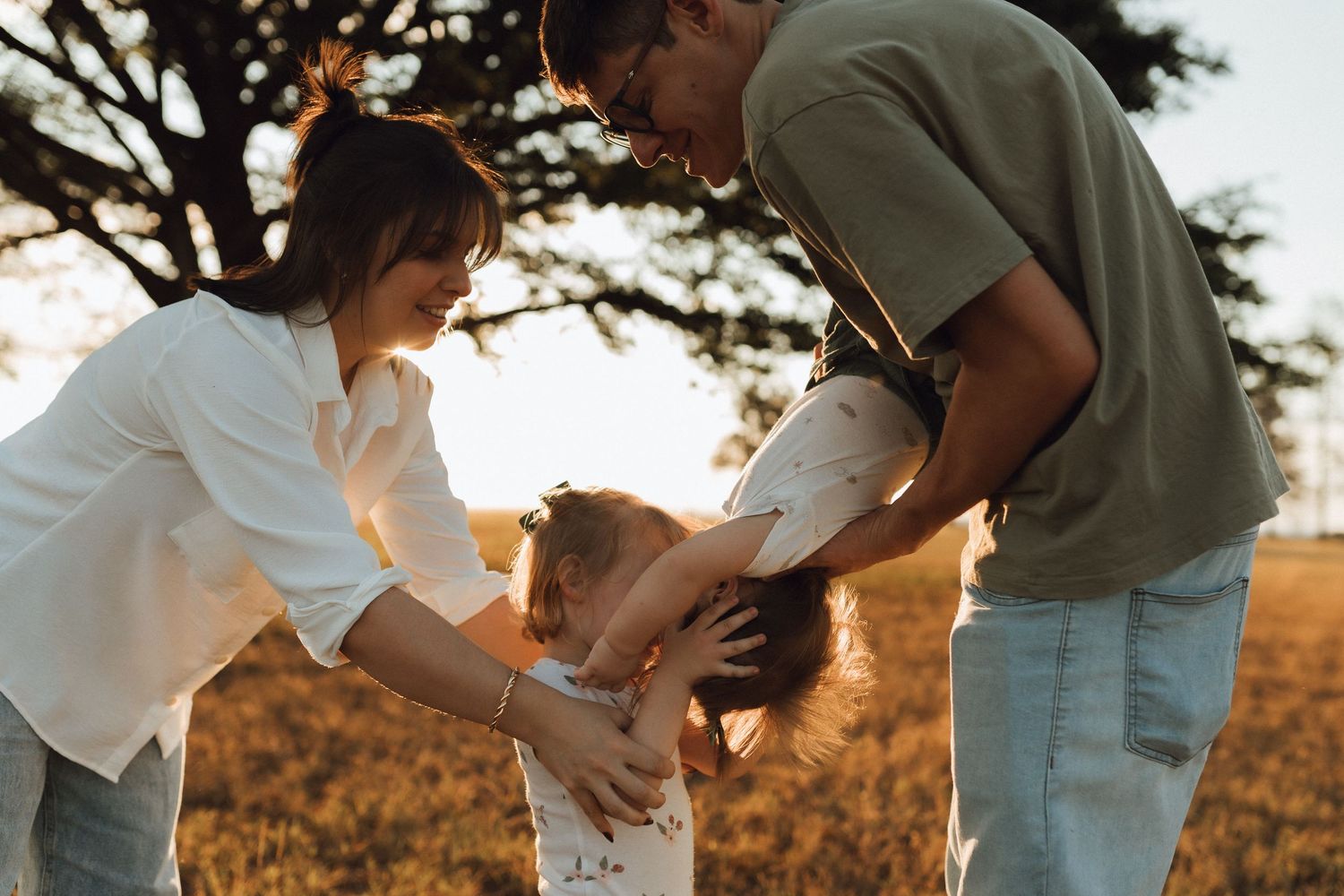 Parents lovingly playing with their young child in a golden field at sunset.