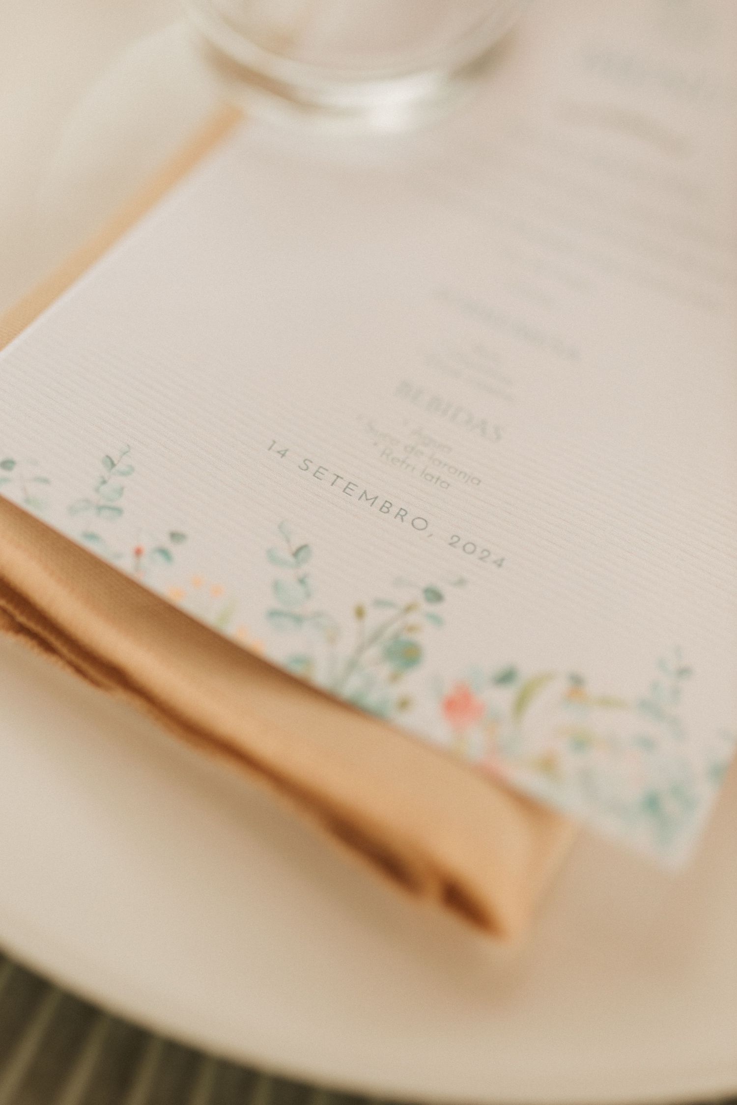 Close-up of elegant wedding menu card with floral border dated 14 Setembro 2024 on a beige linen napkin.