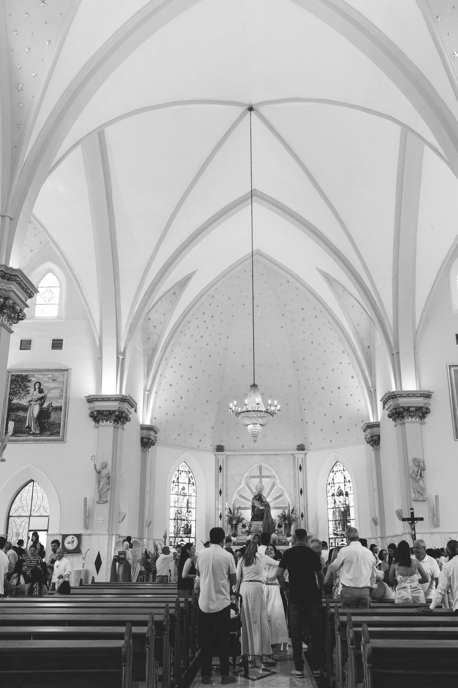 Black and white interior of a Gothic church with vaulted ceilings, pews, and congregation gathered near the altar.