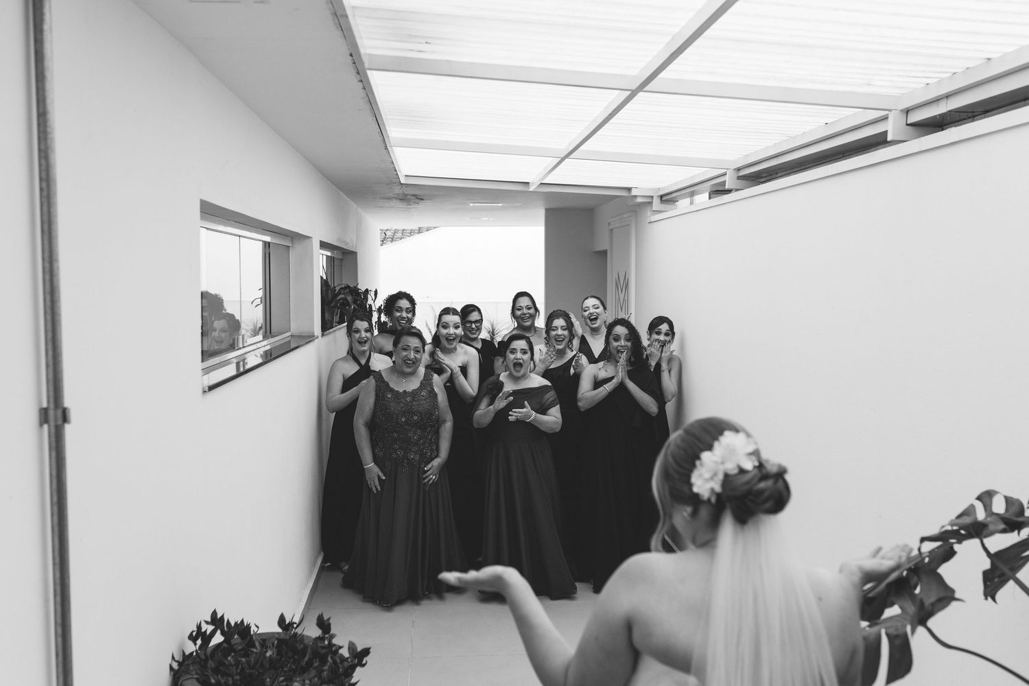 Black and white photo of bridesmaids in dark gowns reacting excitedly upon seeing the bride.