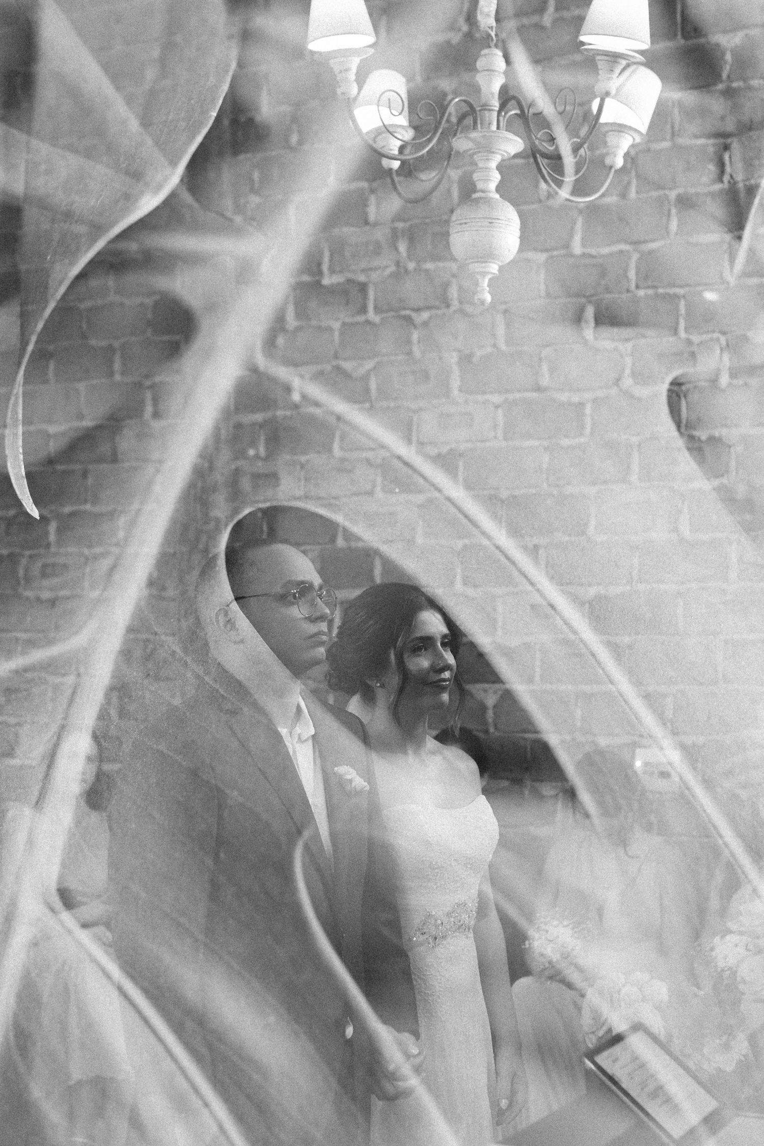 Black and white artistic photo of bride and groom reflected through leaves at rustic brick venue.