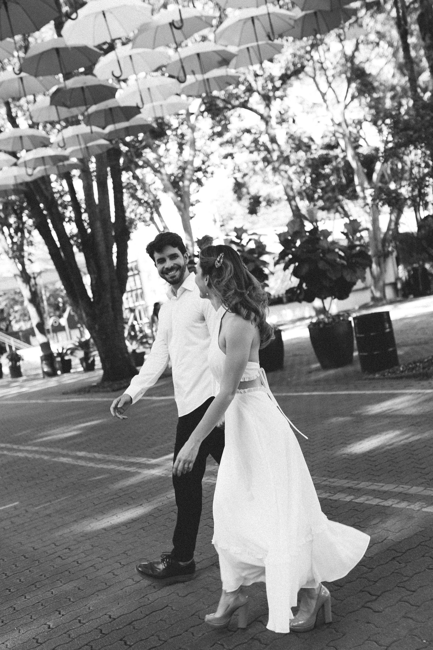 Black and white photo of smiling groom leading bride under umbrella street art.