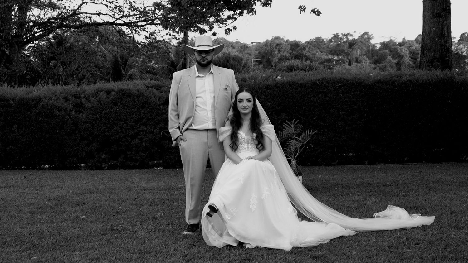 Black and white portrait of bride and groom posing elegantly in a lush garden.