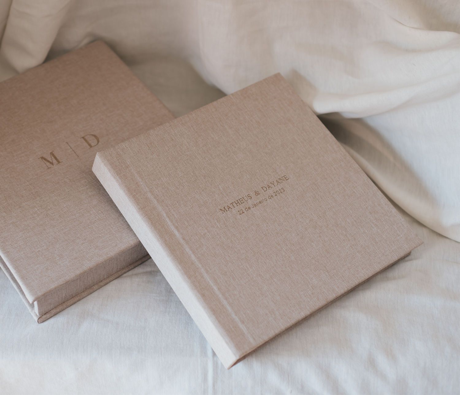 Two elegant linen-covered wedding photo albums with monogram embossing resting on white fabric.
