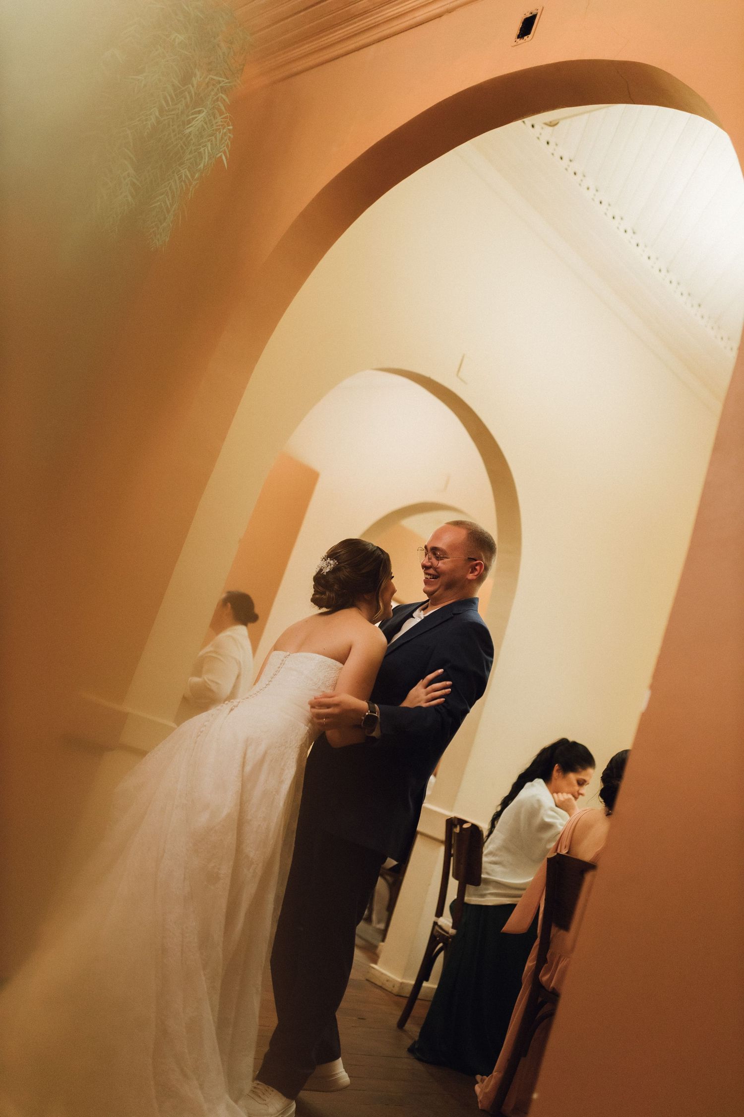 Smiling groom embraces bride in a stunning arched hallway during their wedding reception.