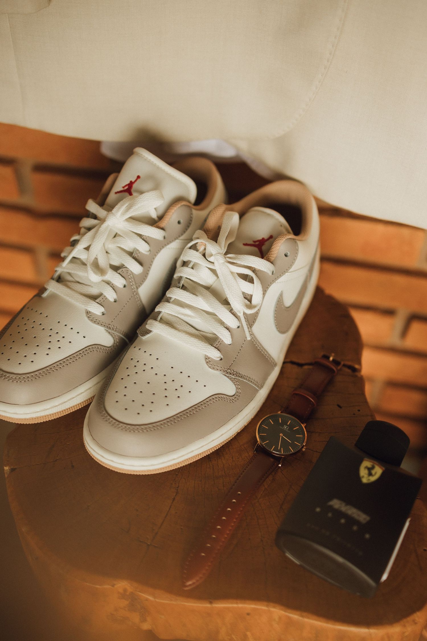 Air Jordan 1 Low sneakers beside a watch and Ferrari cologne on wooden surface for groom.