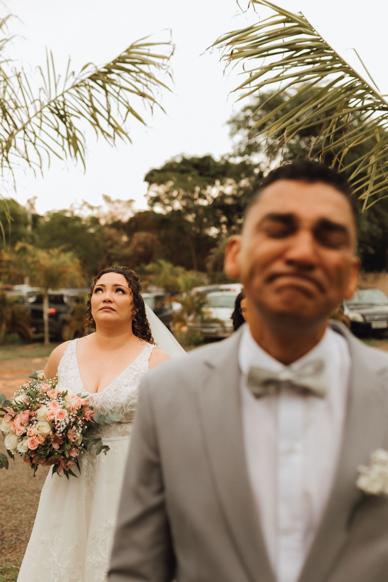 Emotional groom in gray suit reacts as bride holding pink bouquet approaches during first look moment.