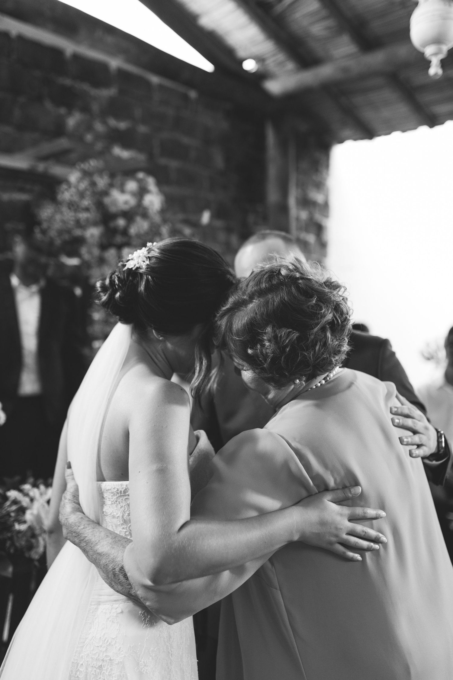 Emotional black and white photo of bride sharing tender embrace with mother after wedding ceremony.