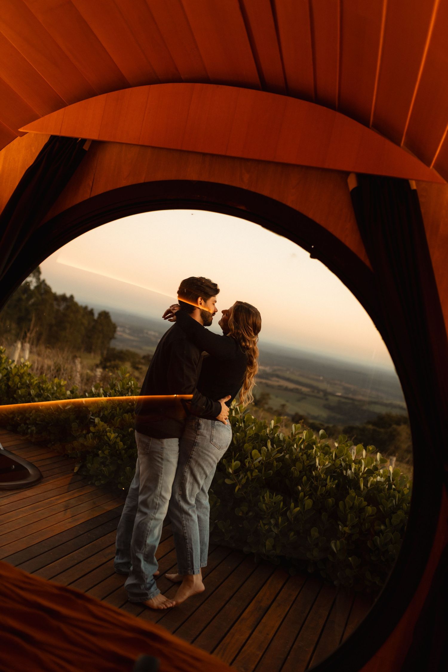 Couple sharing a romantic moment framed by a circular tent opening with a scenic sunset landscape backdrop.