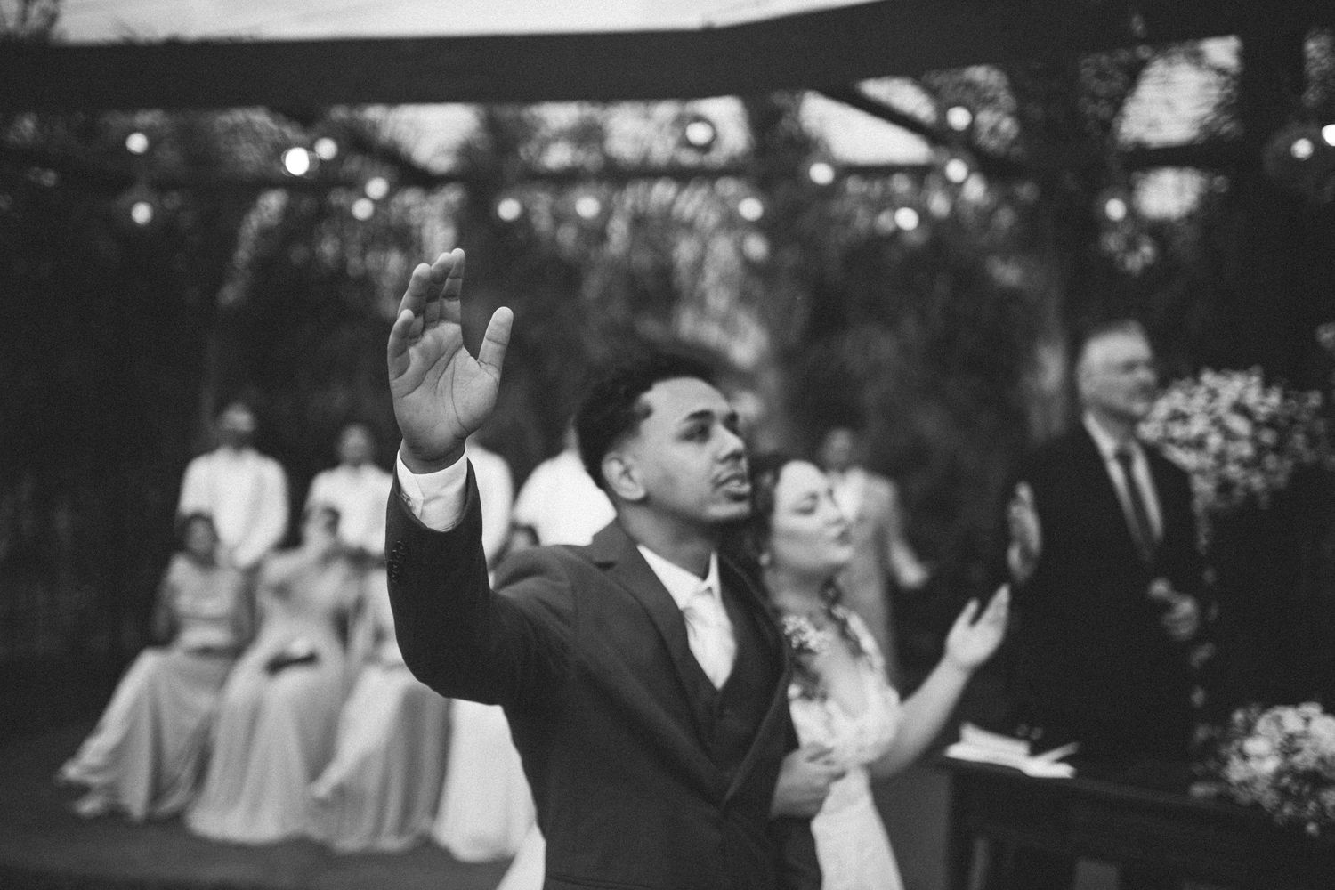 Black and white photo of groom raising hands during emotional outdoor wedding ceremony.