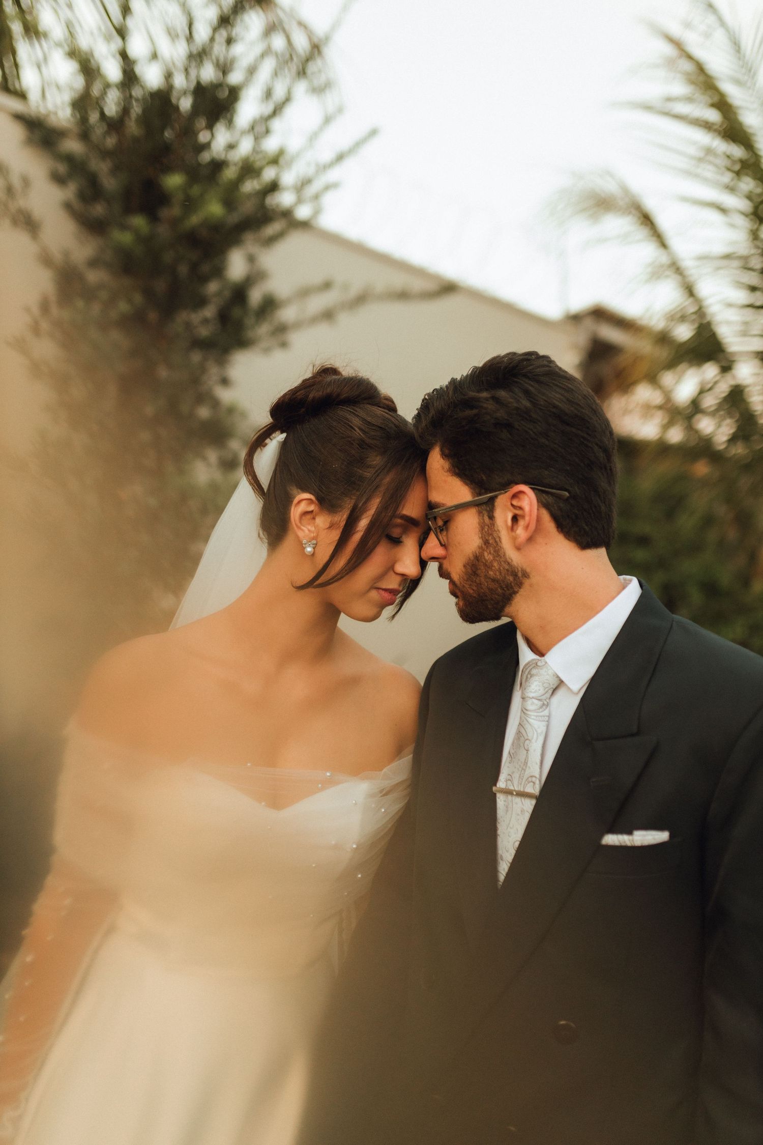 Bride and groom touching foreheads in tender moment at golden hour outdoor wedding.