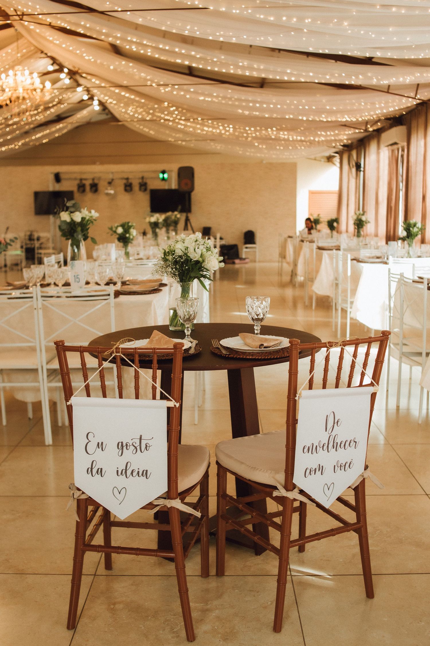 Elegant wedding reception venue with fairy lights, draped ceiling, and decorated bride and groom chairs.