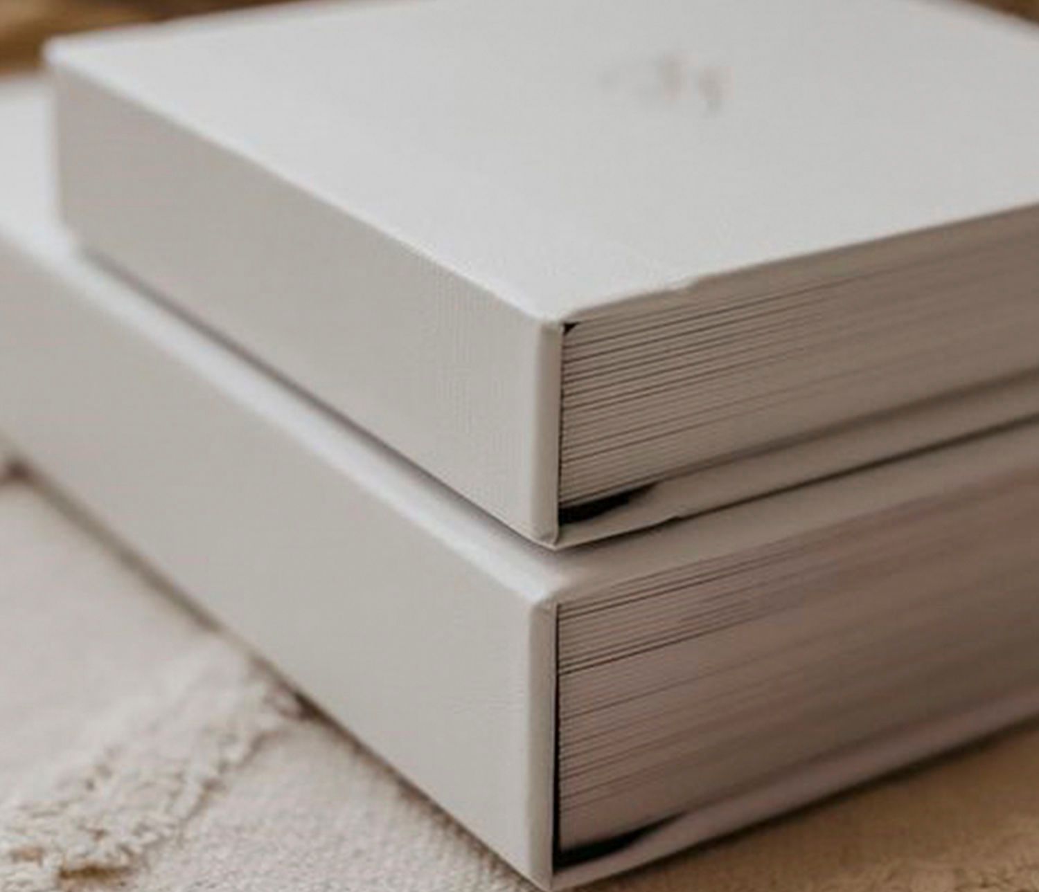 Two elegant white hardcover photo books stacked on a soft cream surface, showcasing minimalist design.