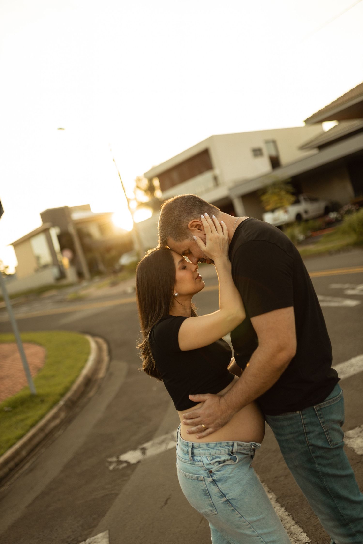 Couple sharing a romantic kiss on a street corner during golden hour sunset in residential neighborhood.