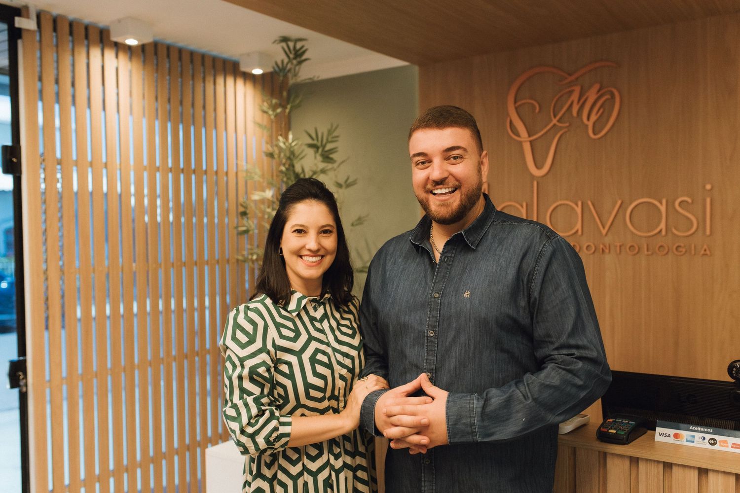 A smiling man and woman pose together at the Lavasi reception desk in a modern, warmly lit office.