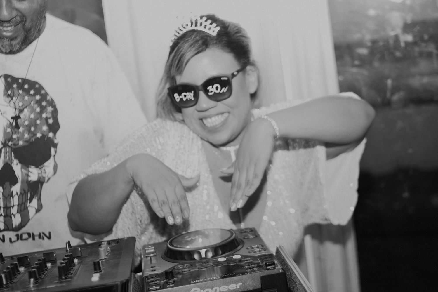 Woman wearing 30th birthday glasses and tiara DJing at a party in black and white photo.