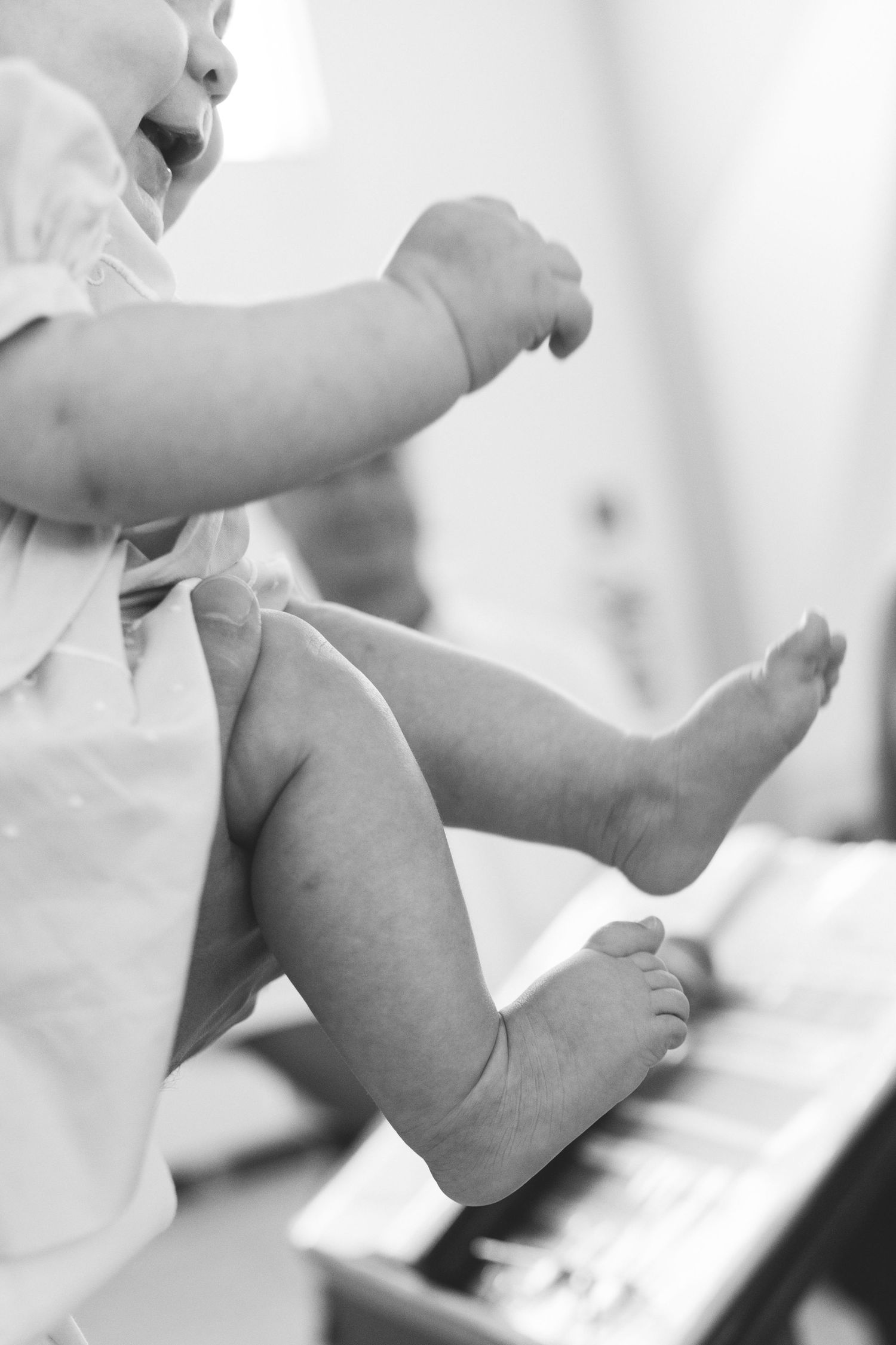 Black and white close-up of a baby's chubby legs and feet while being held by an adult.