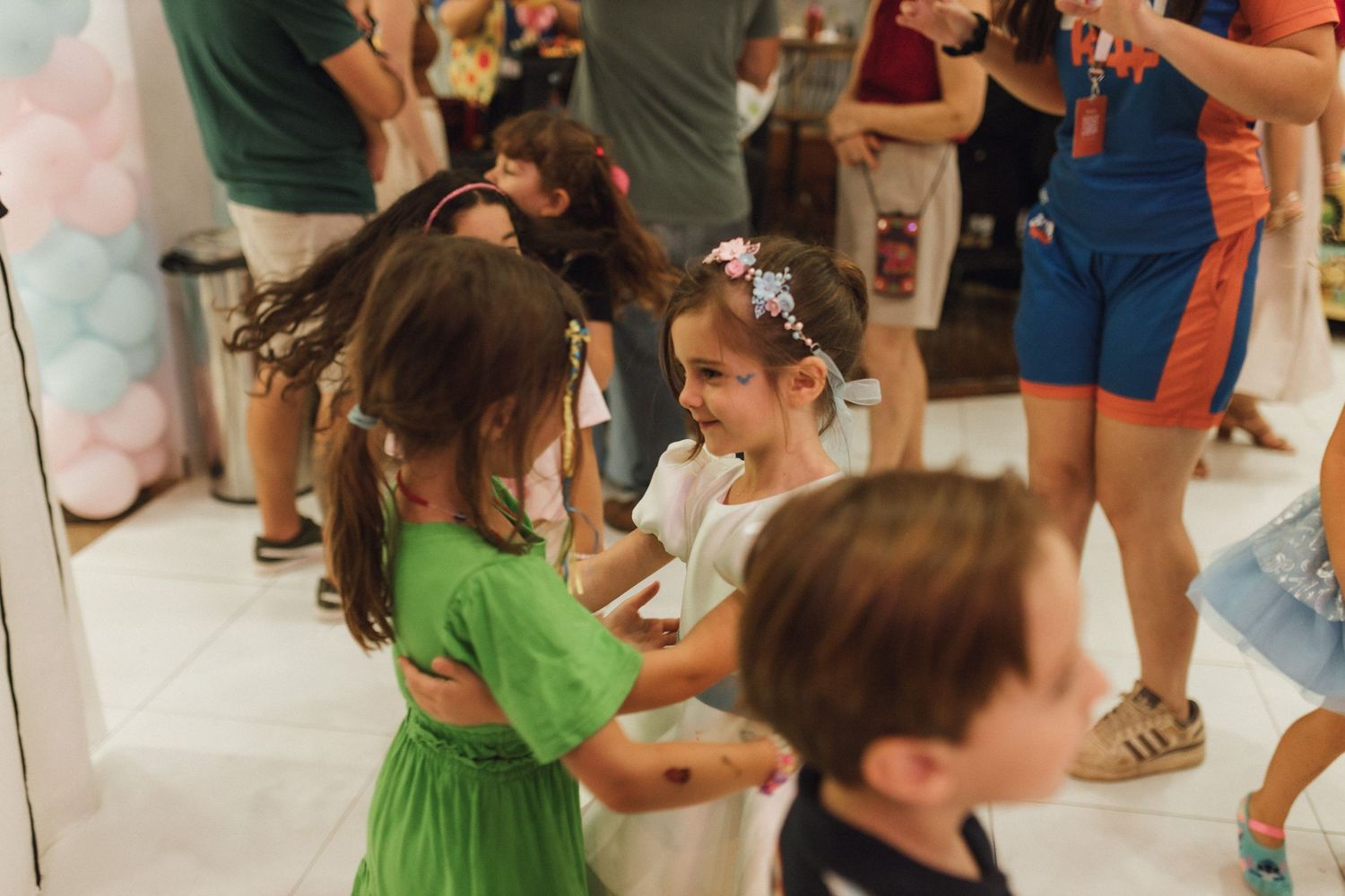 Children dancing and laughing together at a colorful birthday party with balloon decorations in the background.