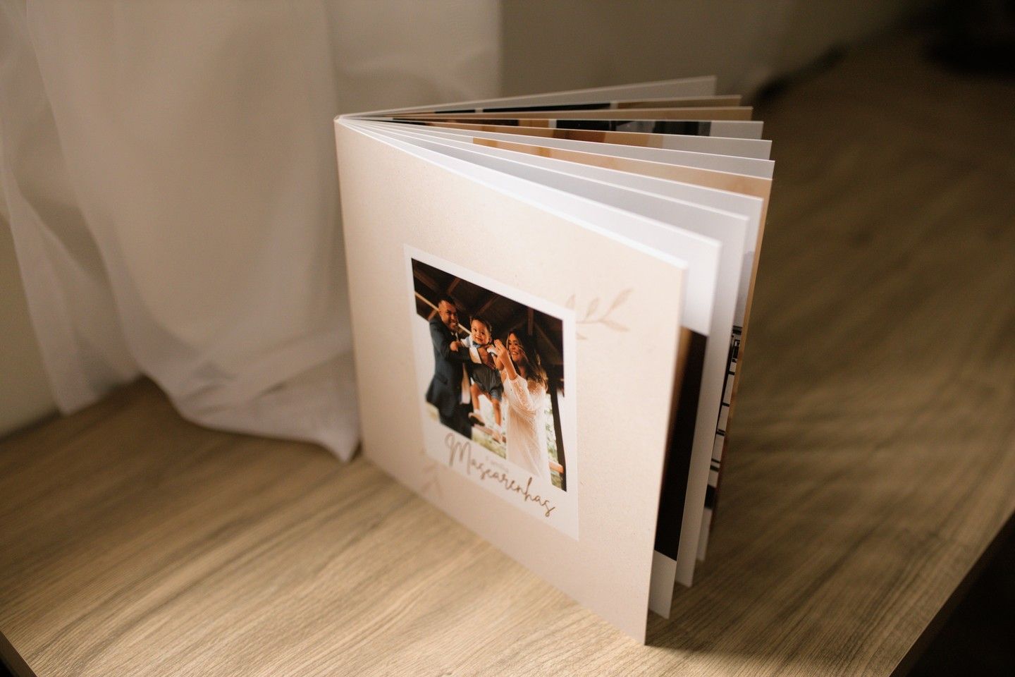 Elegant wedding photo album open on a wooden table, displaying a couple's special moments in a soft white cover.