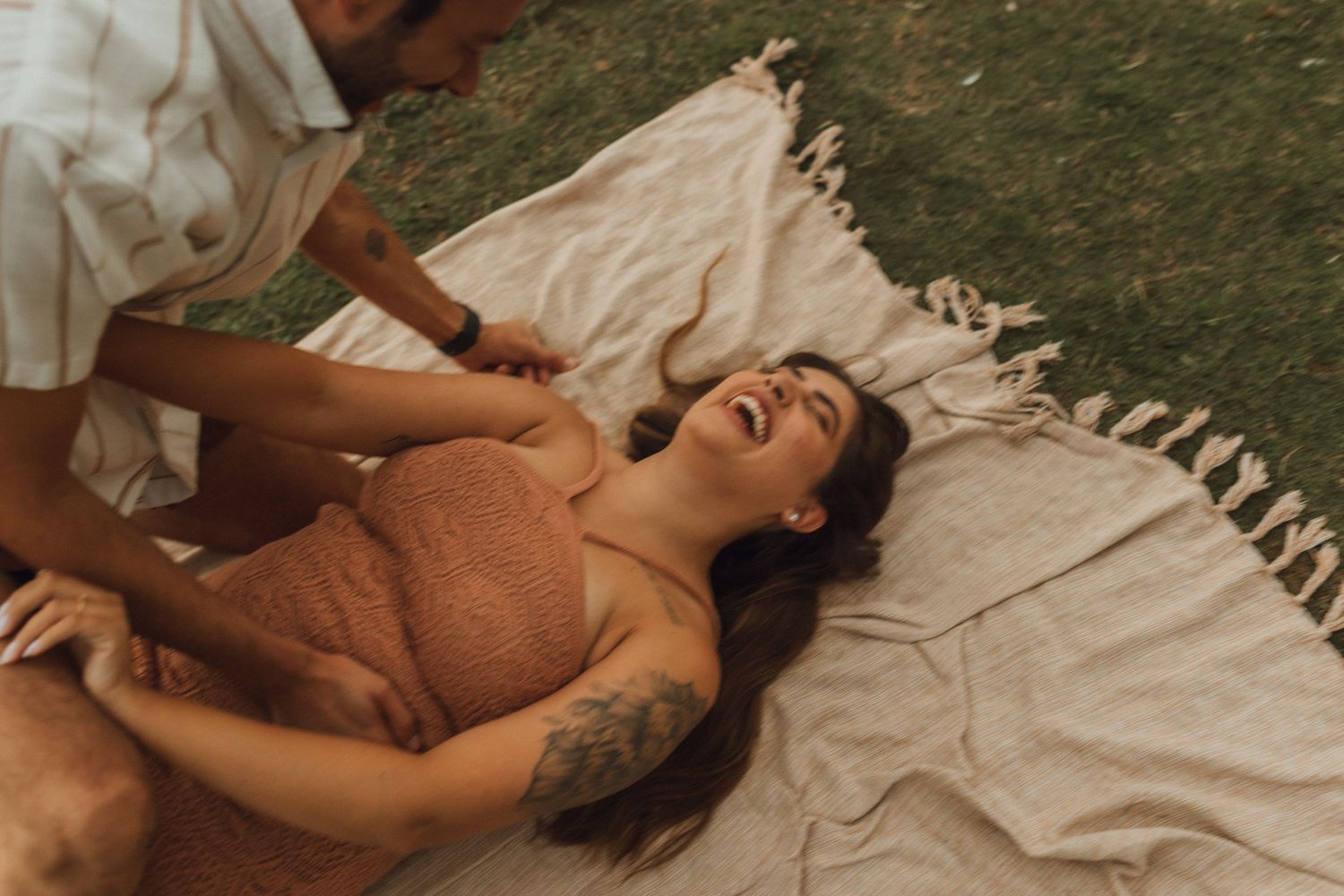 Woman in rust dress laughing while lying on blanket outdoors.
