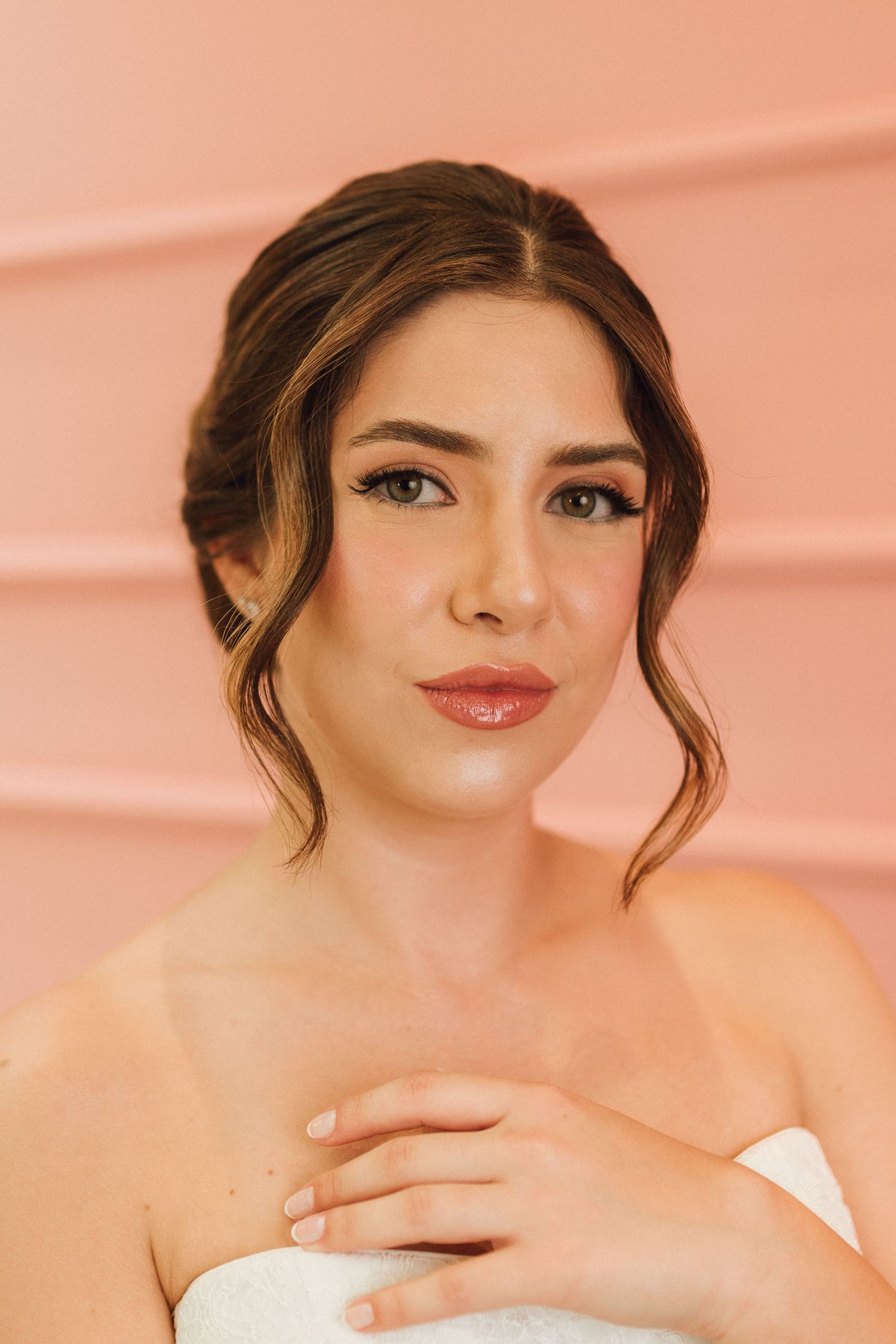 Elegant bride with upswept hair and natural makeup posing against a soft pink background.