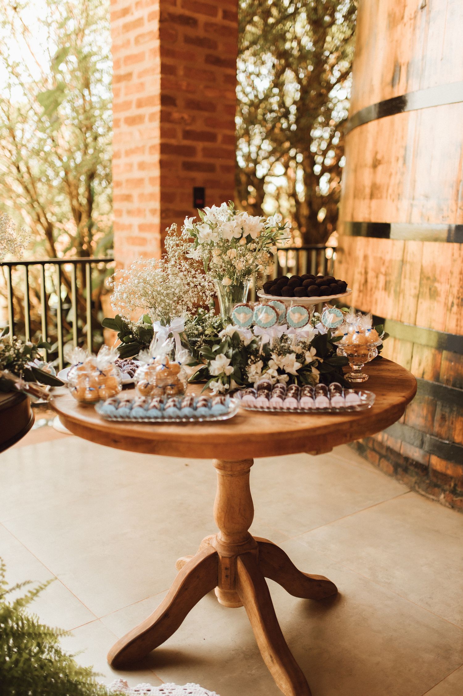 Elegant wooden pedestal table displaying floral arrangements and desserts on a sunlit outdoor patio.