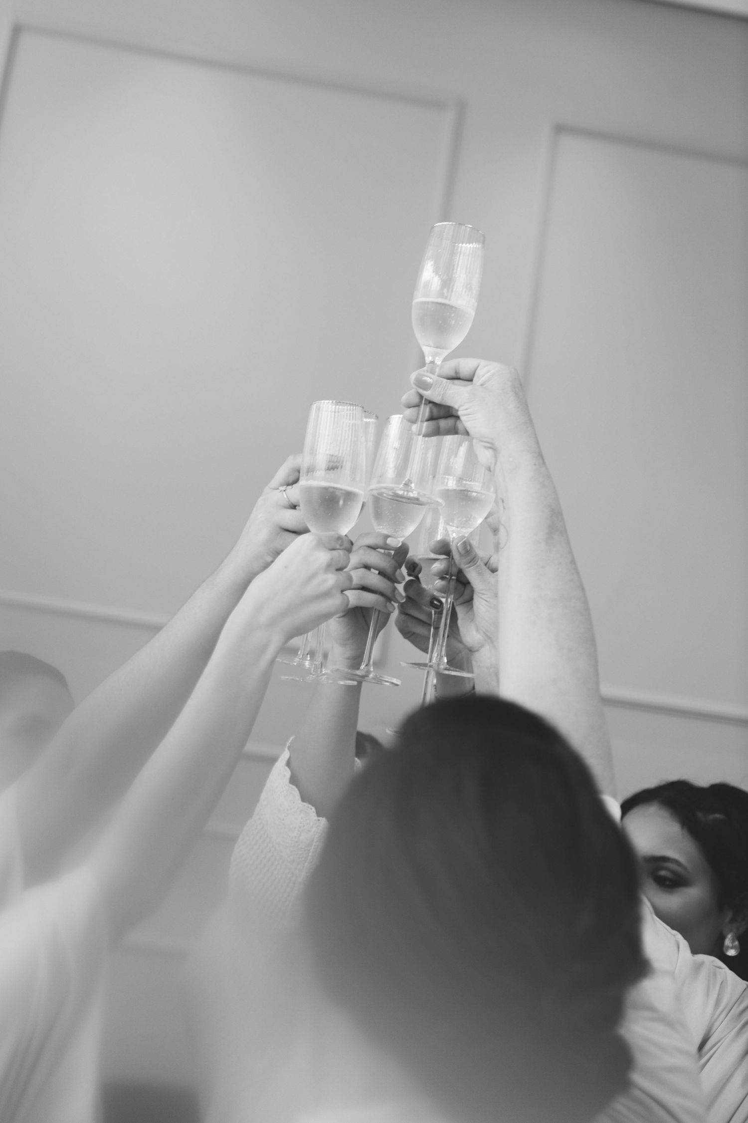 Black and white photo of wedding party raising champagne glasses in a celebratory toast.