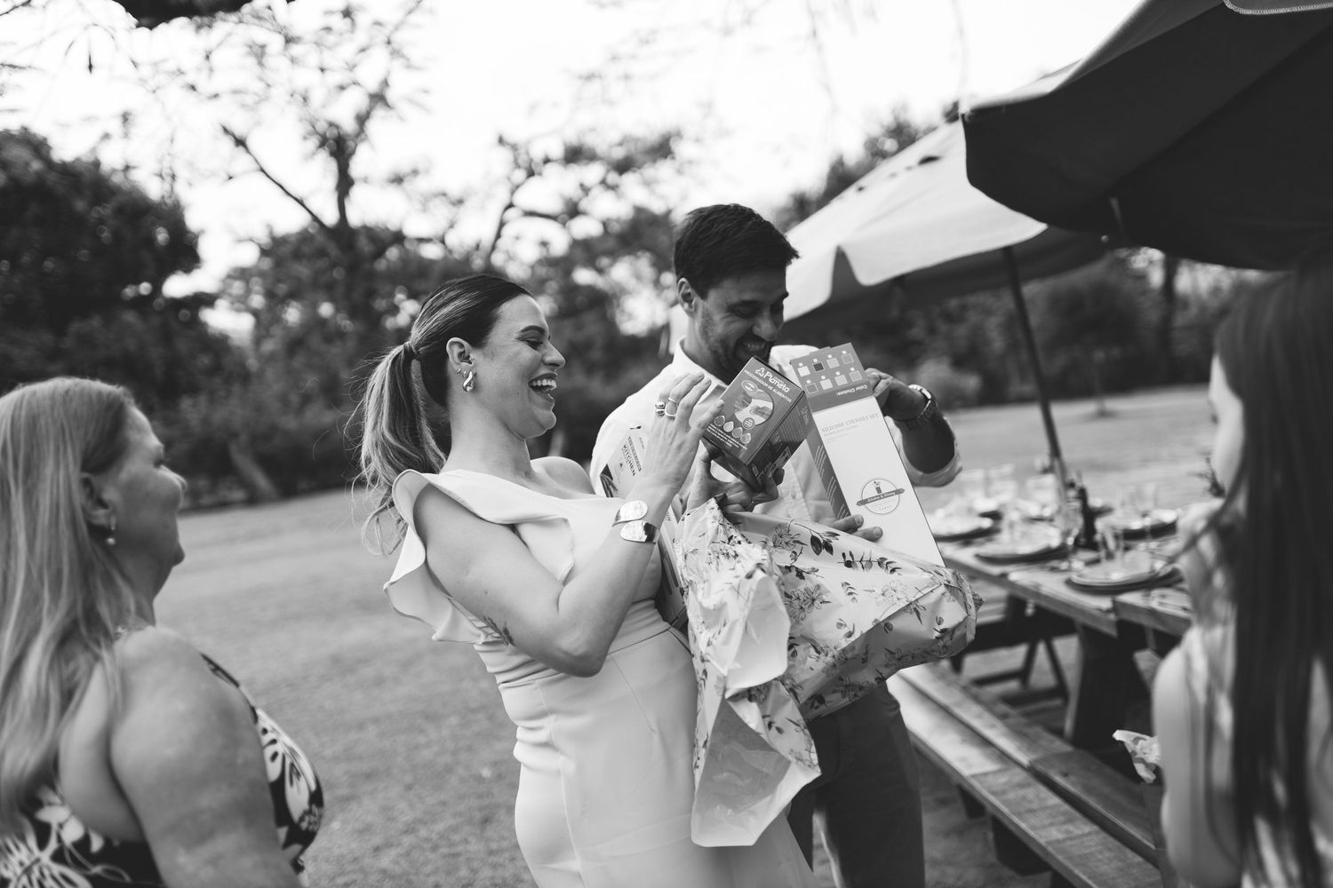 Black and white photo of a couple opening gifts outdoors at a garden party celebration.