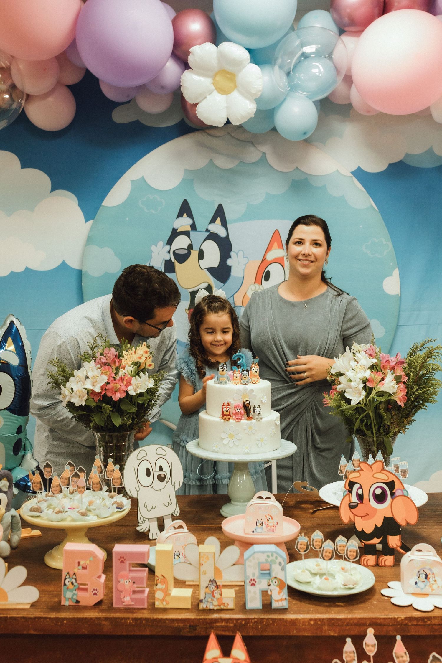 Family celebrating a Bluey-themed birthday party with cake and balloon decorations.