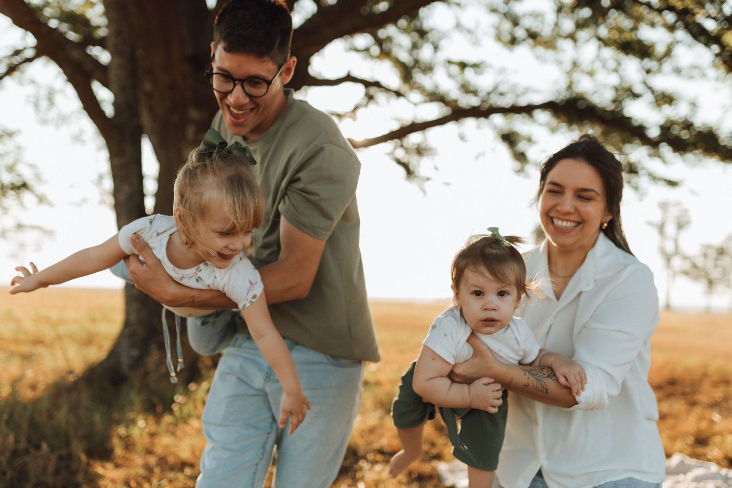 Joyful family with two young children playing outdoors in a golden field at sunset.
