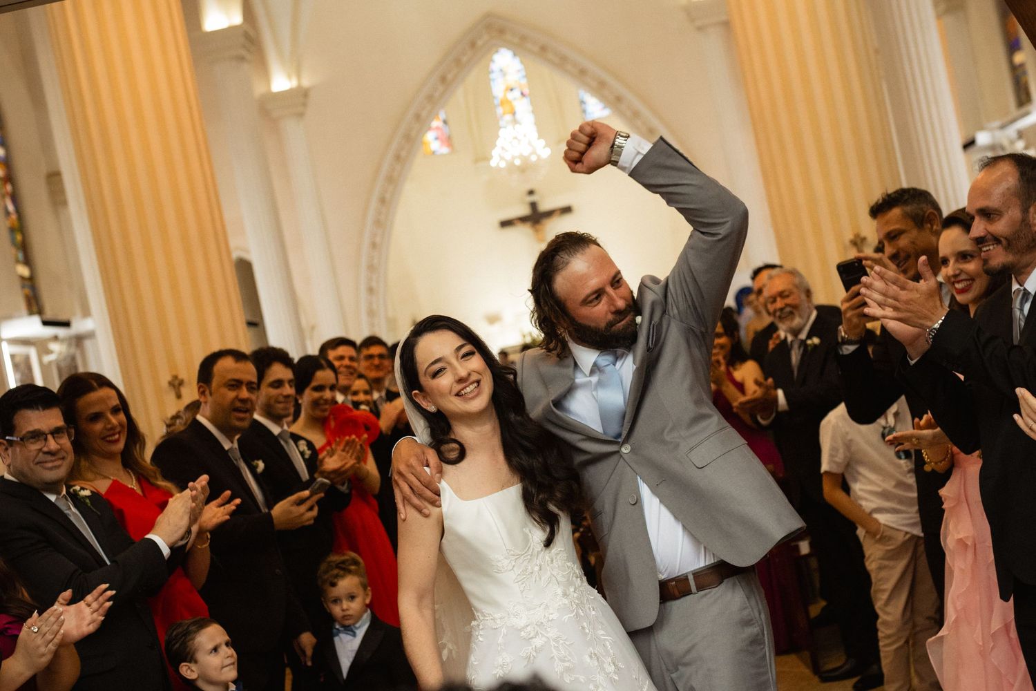 Joyful newlyweds celebrate their wedding ceremony exit in a church, surrounded by cheering guests.