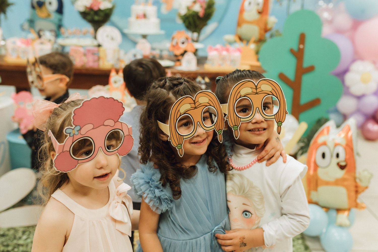 Three children wearing Bluey character photo booth glasses at a colorful birthday party celebration.