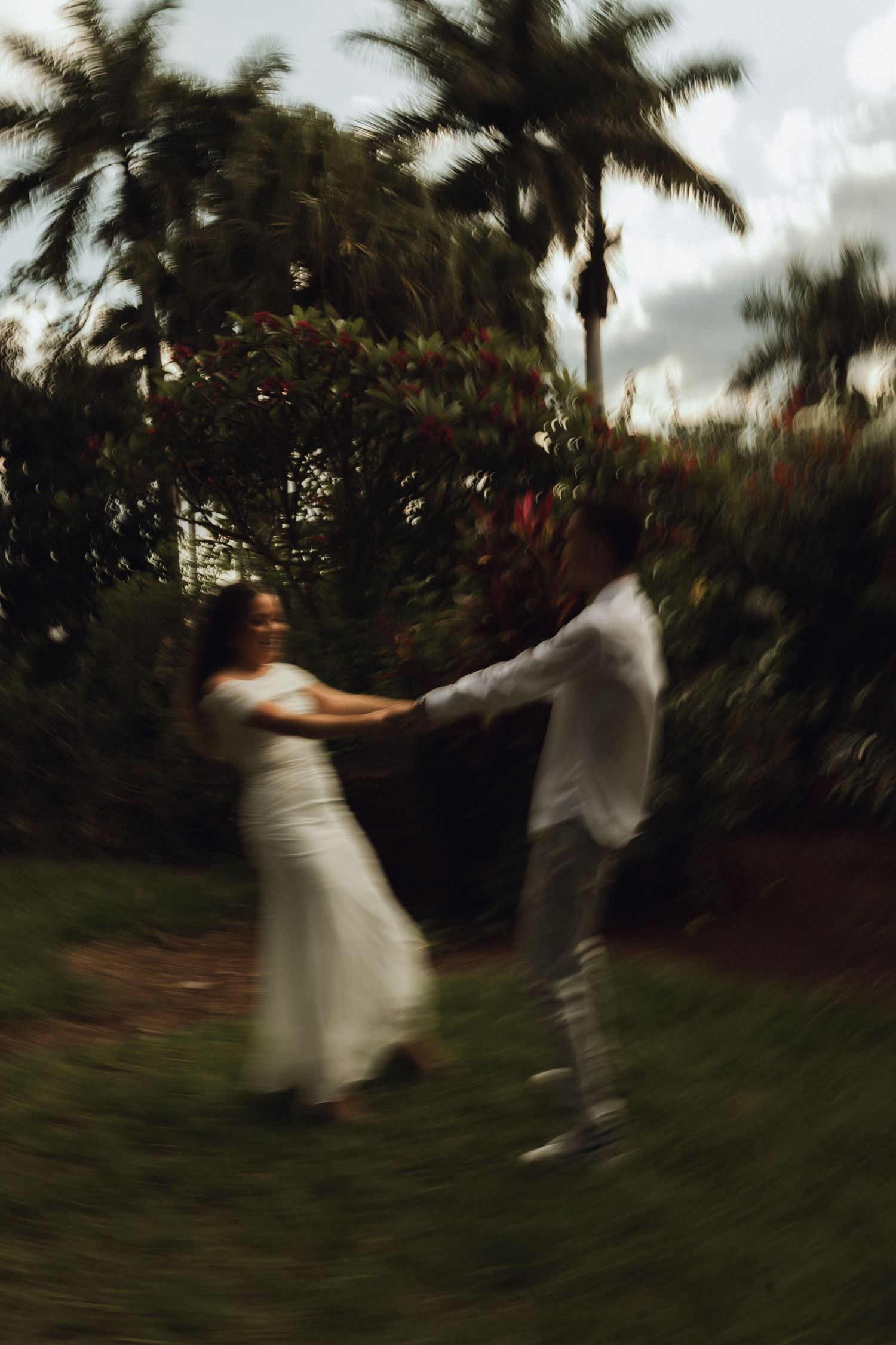 Blurred motion photo of a joyful couple dancing and spinning together in a lush tropical garden.