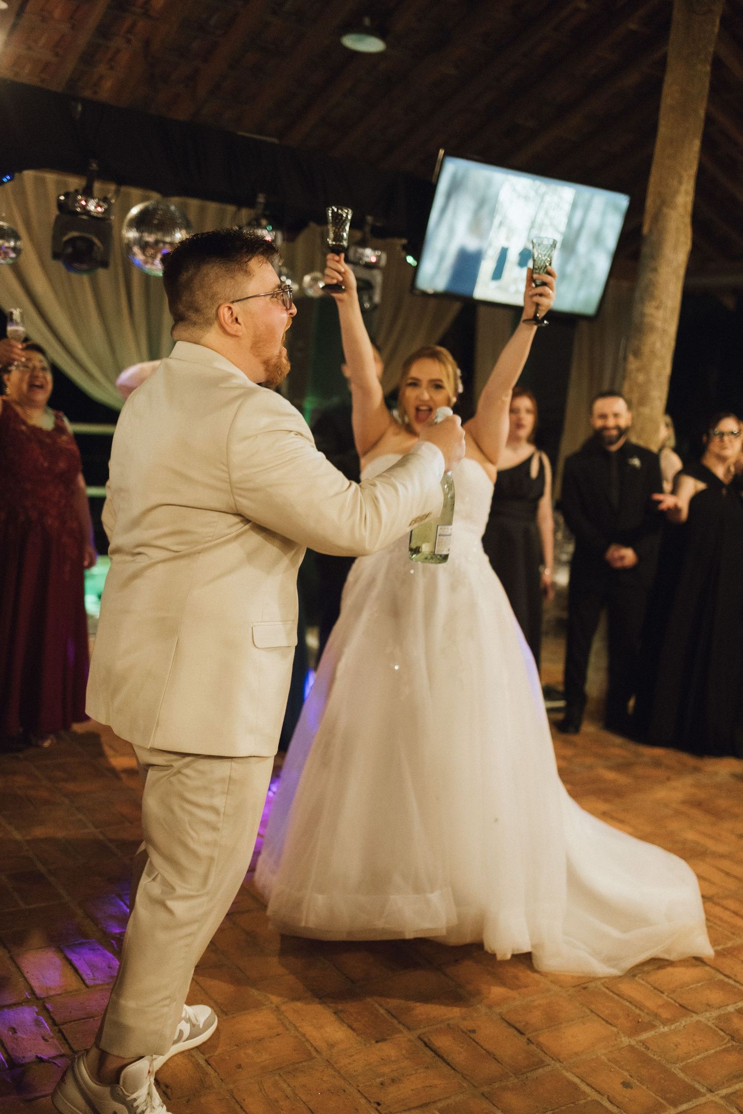 Bride and groom celebrating at wedding reception, raising glasses in a toast on the dance floor.