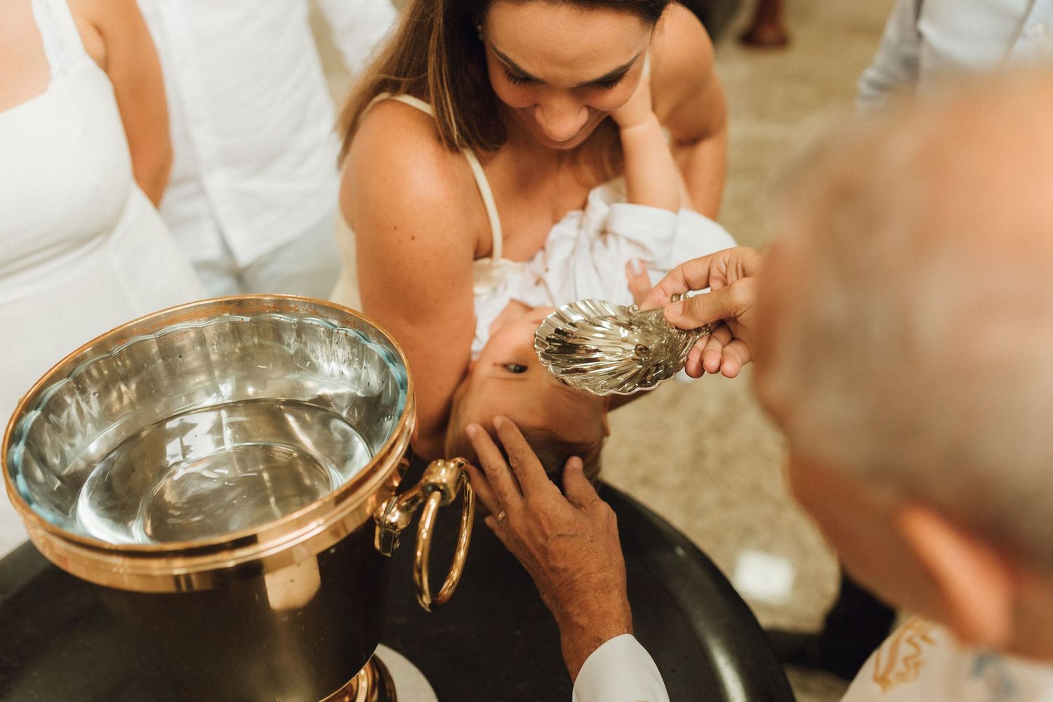 Priest baptizing a baby at a golden font, with mother holding infant during a Christian baptism ceremony.