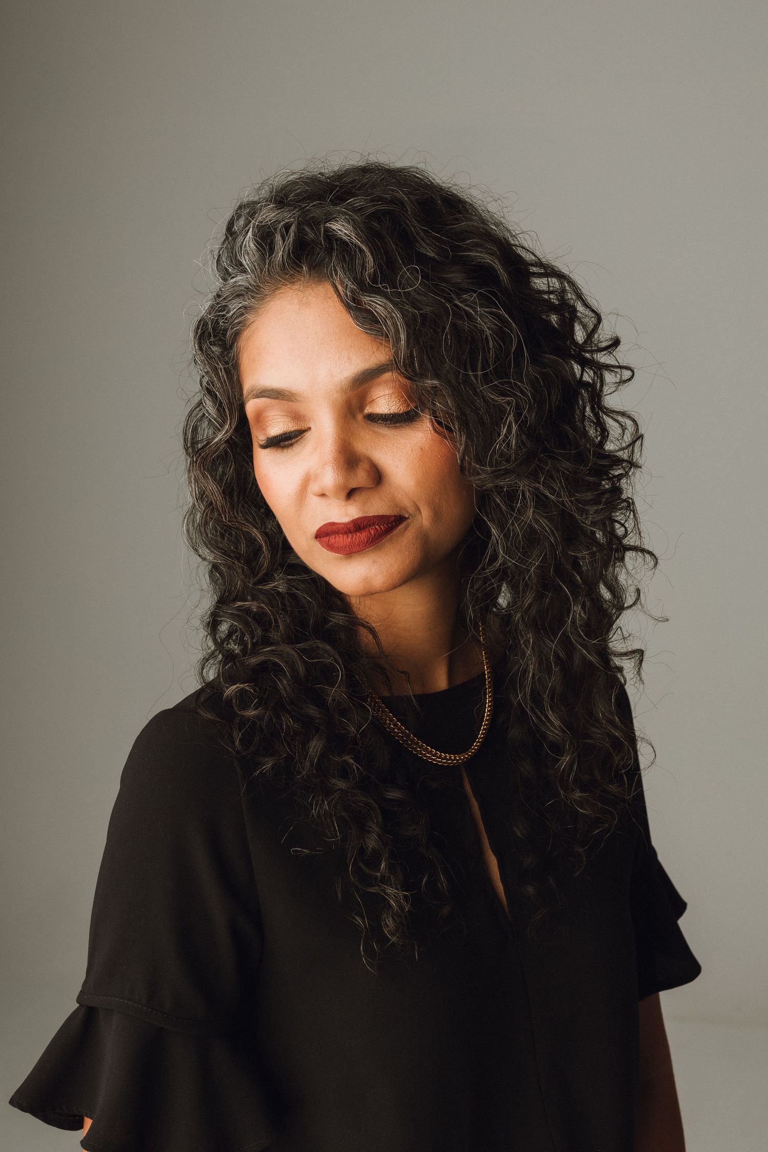 Woman with curly hair in black dress with eyes closed portrait.