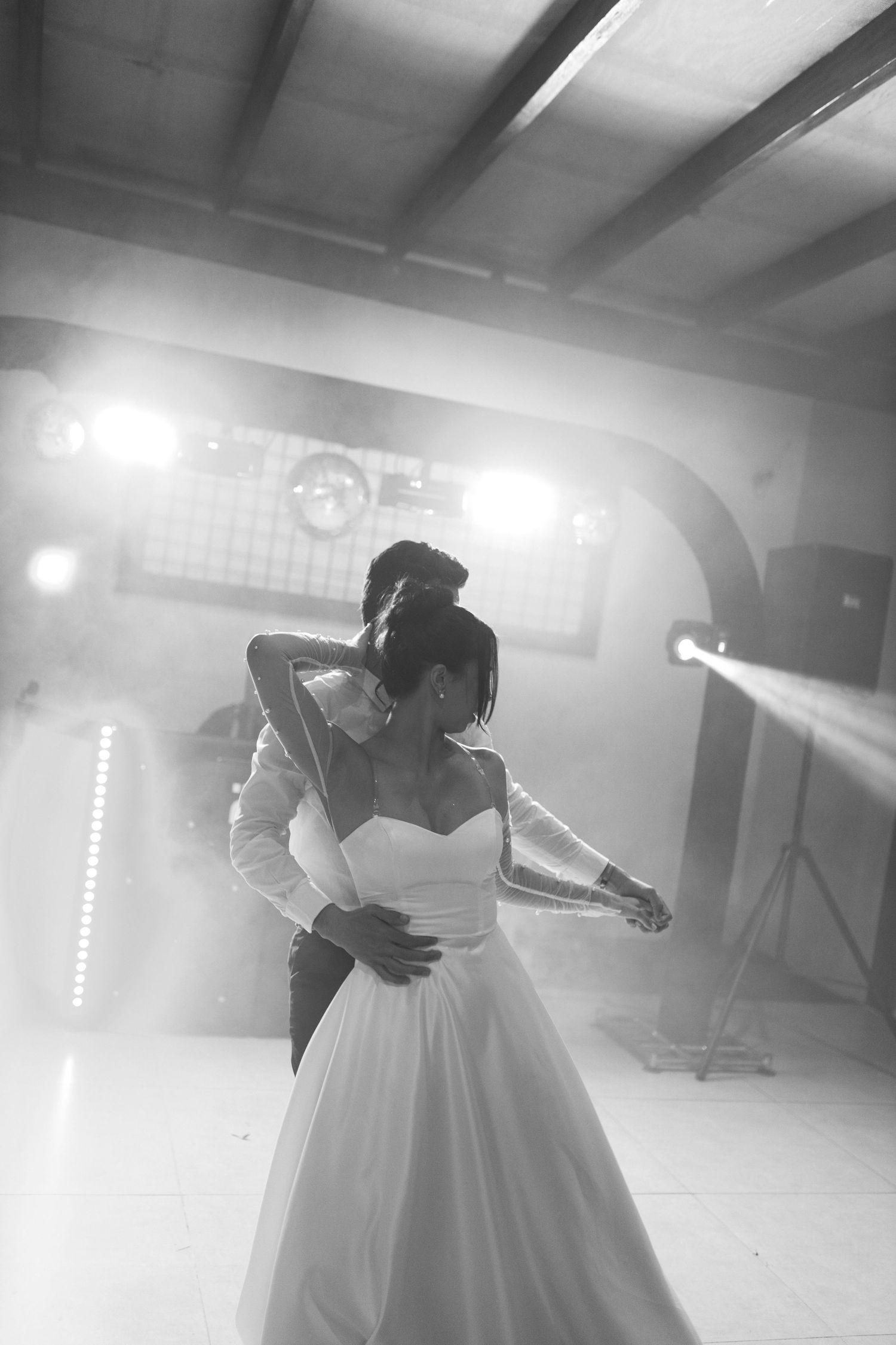 Bride and groom share their first dance in black and white wedding photo with dramatic stage lighting.