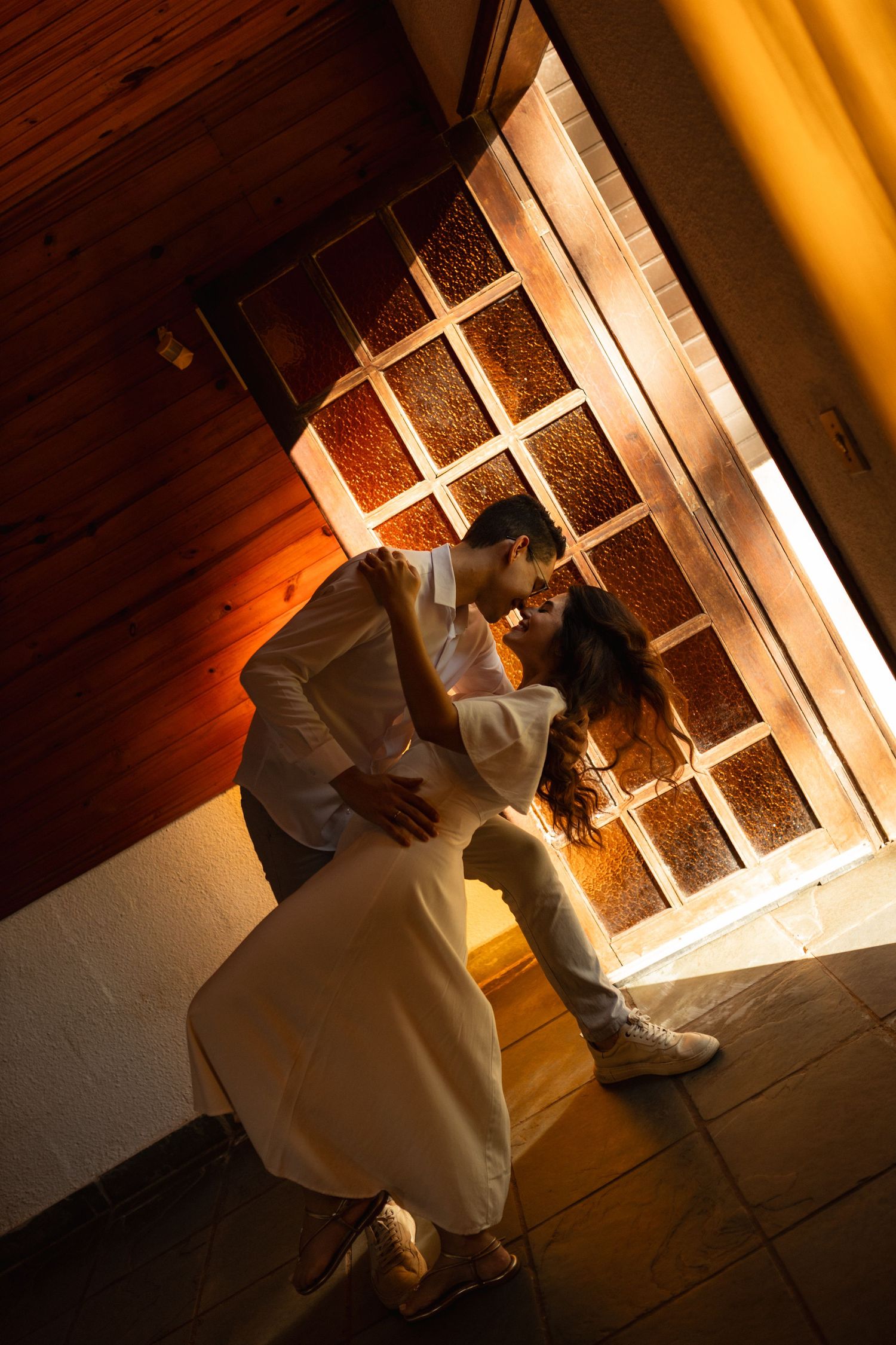 Couple sharing a romantic embrace near a glowing stained glass window in warm golden light.