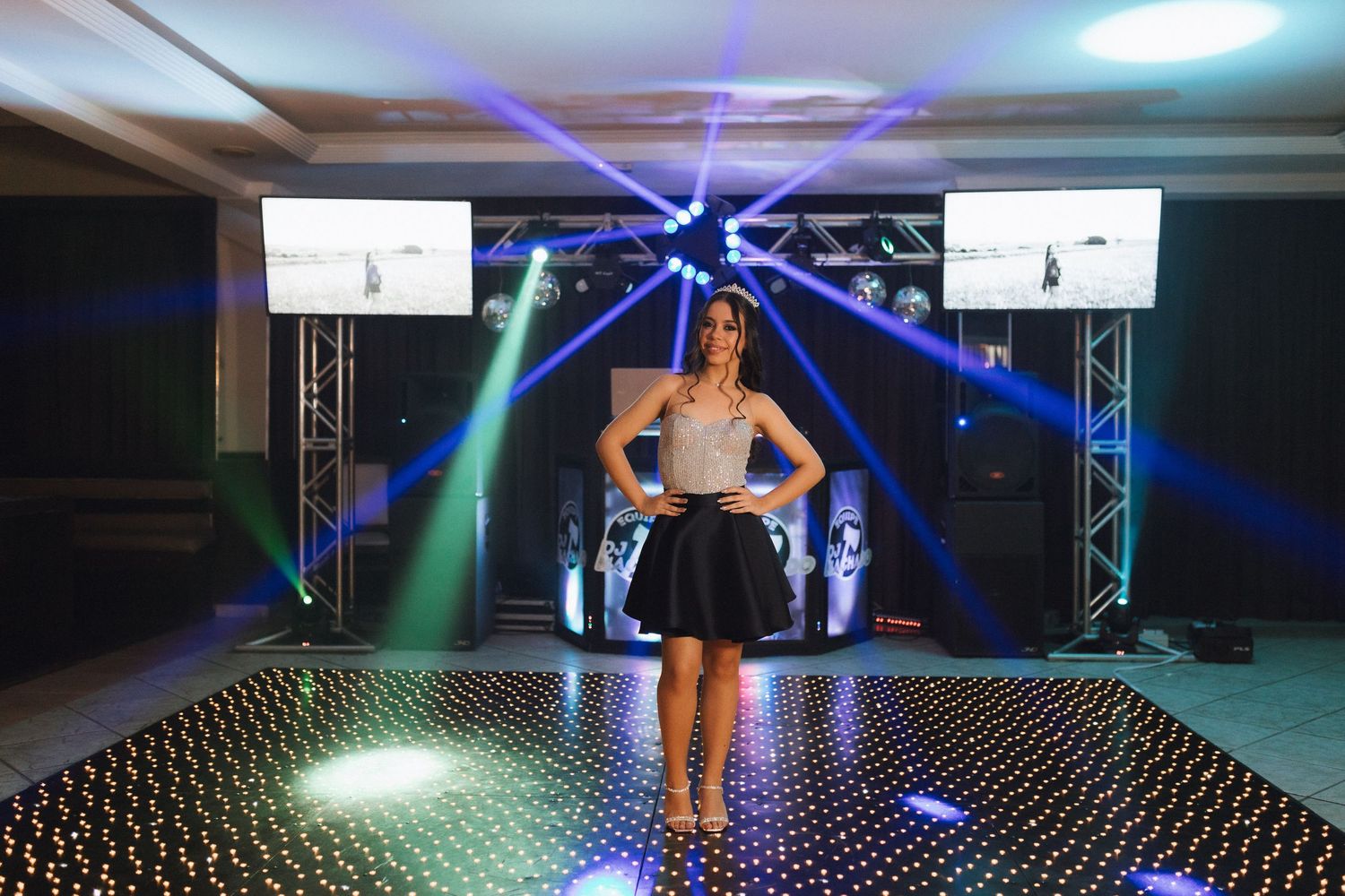 Young woman in black skirt poses on sparkling dance floor with colorful stage lights at elegant party venue.
