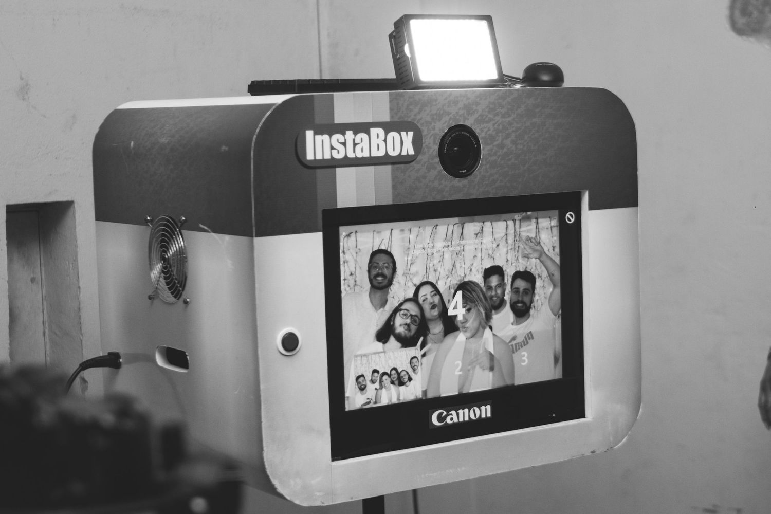InstaBox photo booth with Canon camera displaying a group selfie, featuring a built-in flash and screen.