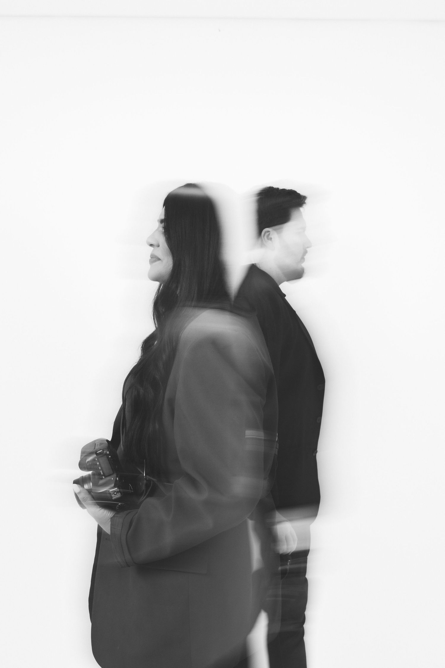 Blurred black and white photo of a man and woman standing back to back against a white wall.