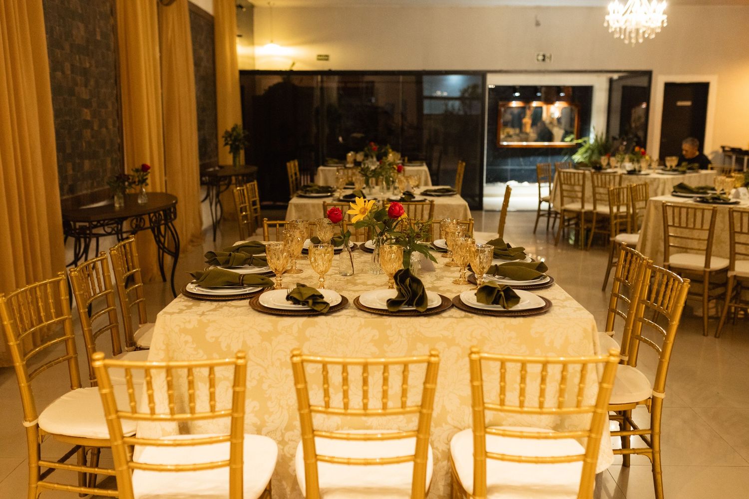Elegant banquet hall with gold Chiavari chairs, white linen tables, floral centerpieces, and warm lighting for a formal event.