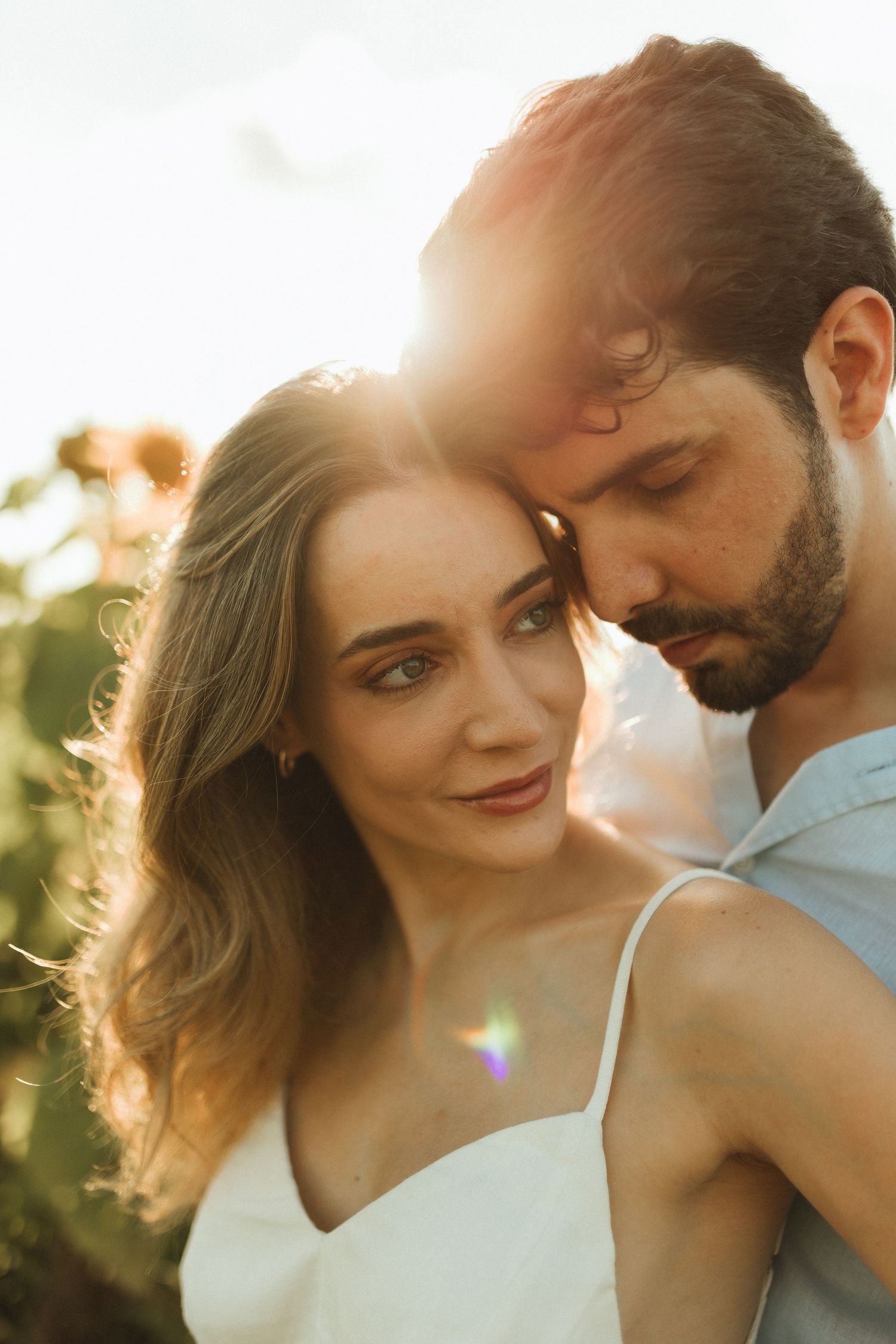 Couple sharing intimate moment with man nuzzling woman's head in golden sunflower field at sunset.
