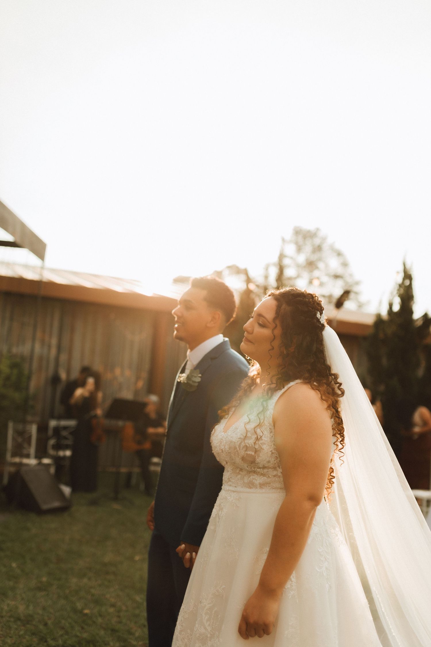 Bride and groom stand together in golden sunset light at elegant outdoor wedding ceremony.