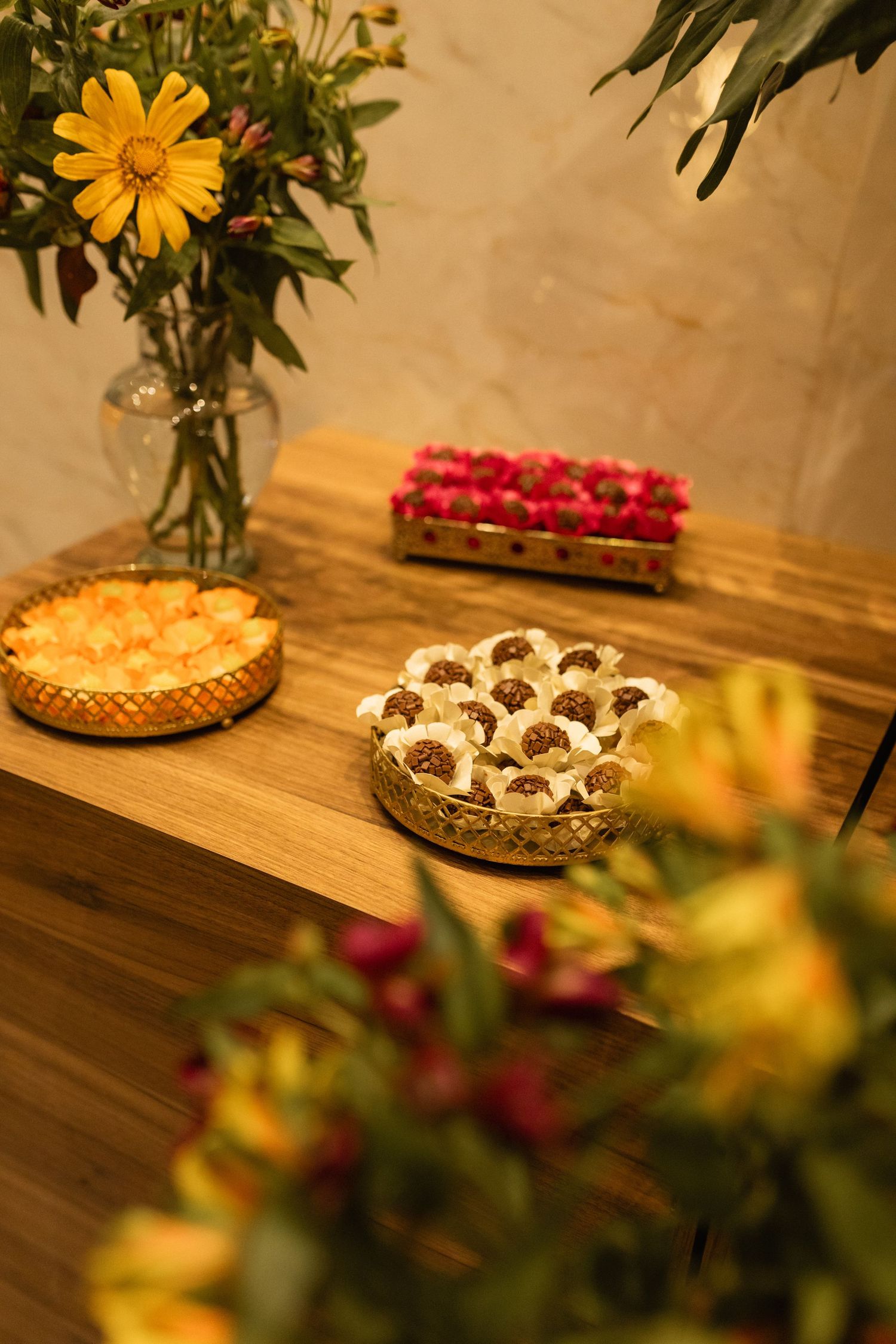 Elegant dessert table with chocolates, fruit tarts, and fresh flowers on a wooden surface.
