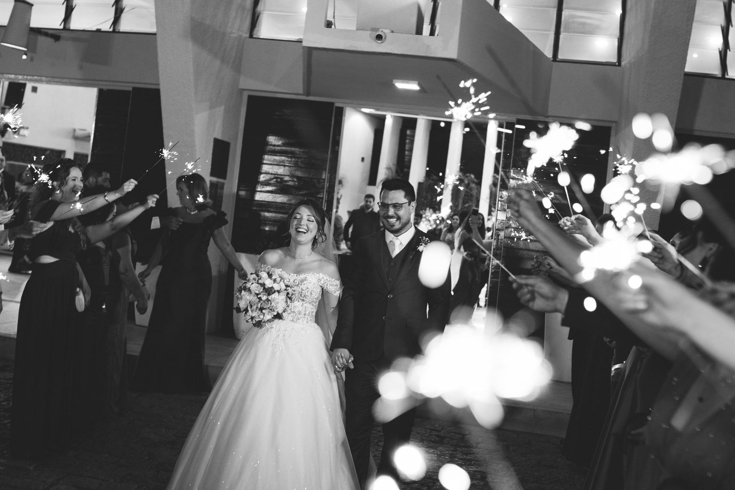 Black and white photo of newlyweds walking through sparkler exit at wedding reception.